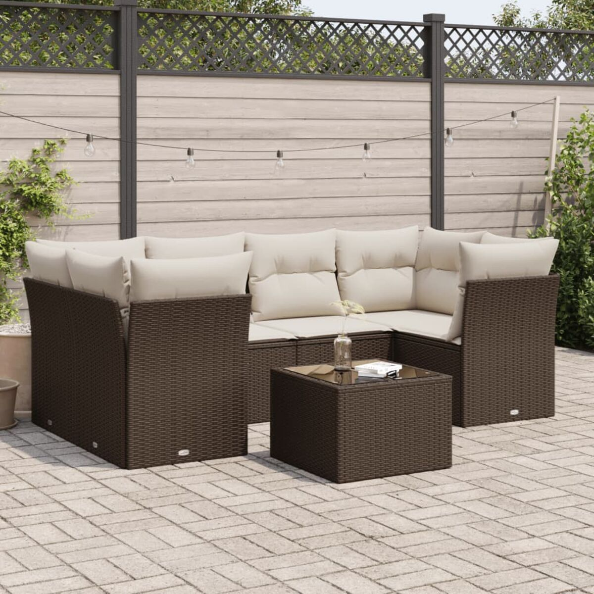 Set di divani da esterno in vimini marrone con cuscini beige, un tavolino, su piastrelle del patio, con una recinzione sullo sfondo.