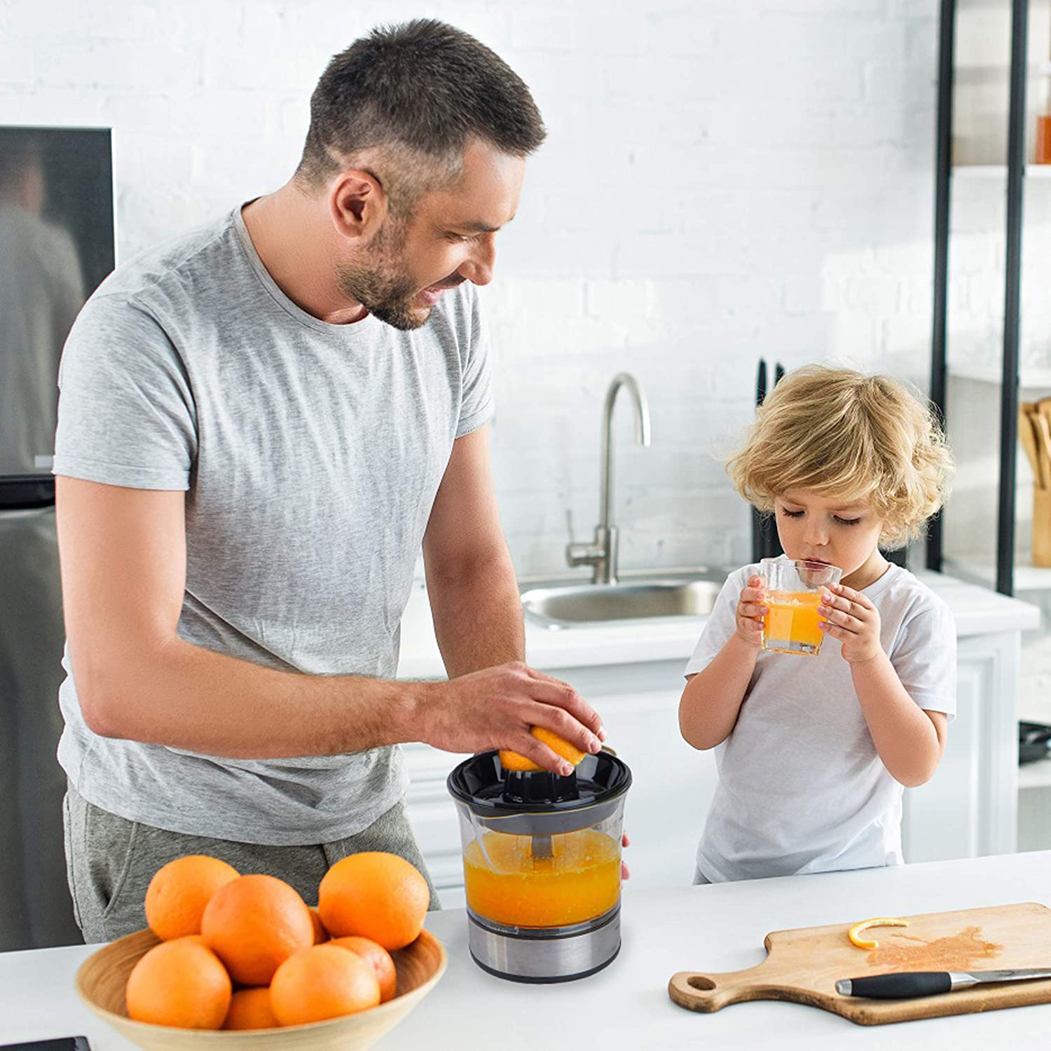 Mann presst Orangensaft, Kind trinkt. Schüssel Orangen, Schneidebrett mit Messer.