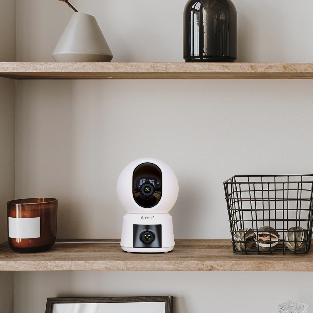 Weiße Smart-Home-Sicherheitskamera auf einem Regal, neben Dekorationen und einer Kerze.