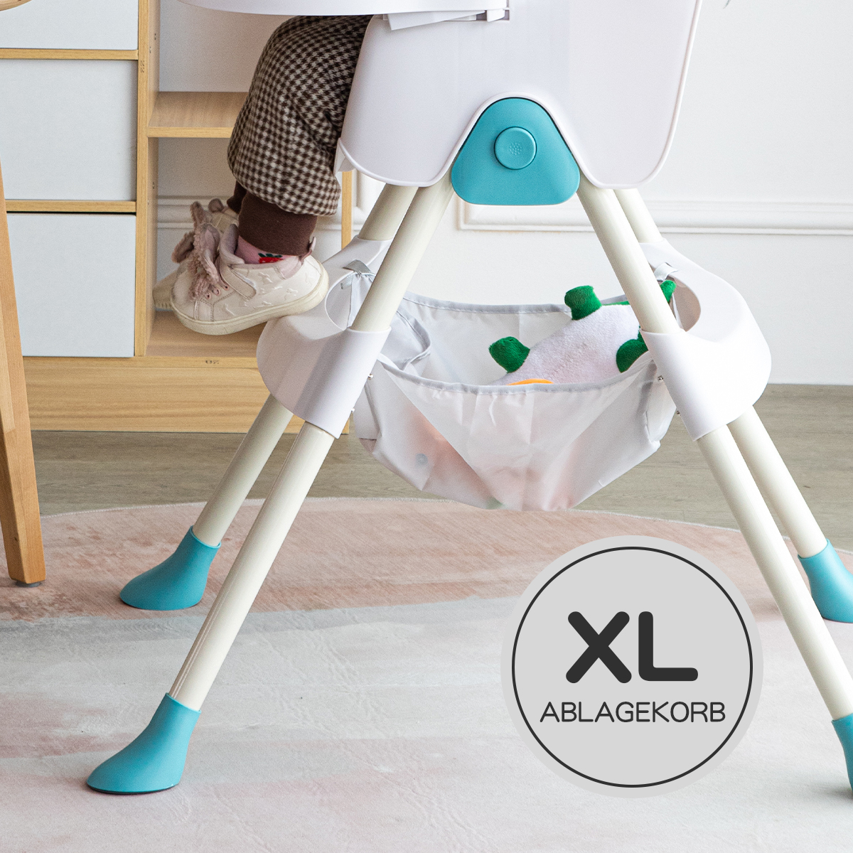 Ein Hochstuhl mit den Beinen und Füßen eines Babys. Ein XL-Ablagekorb befindet sich darunter.
