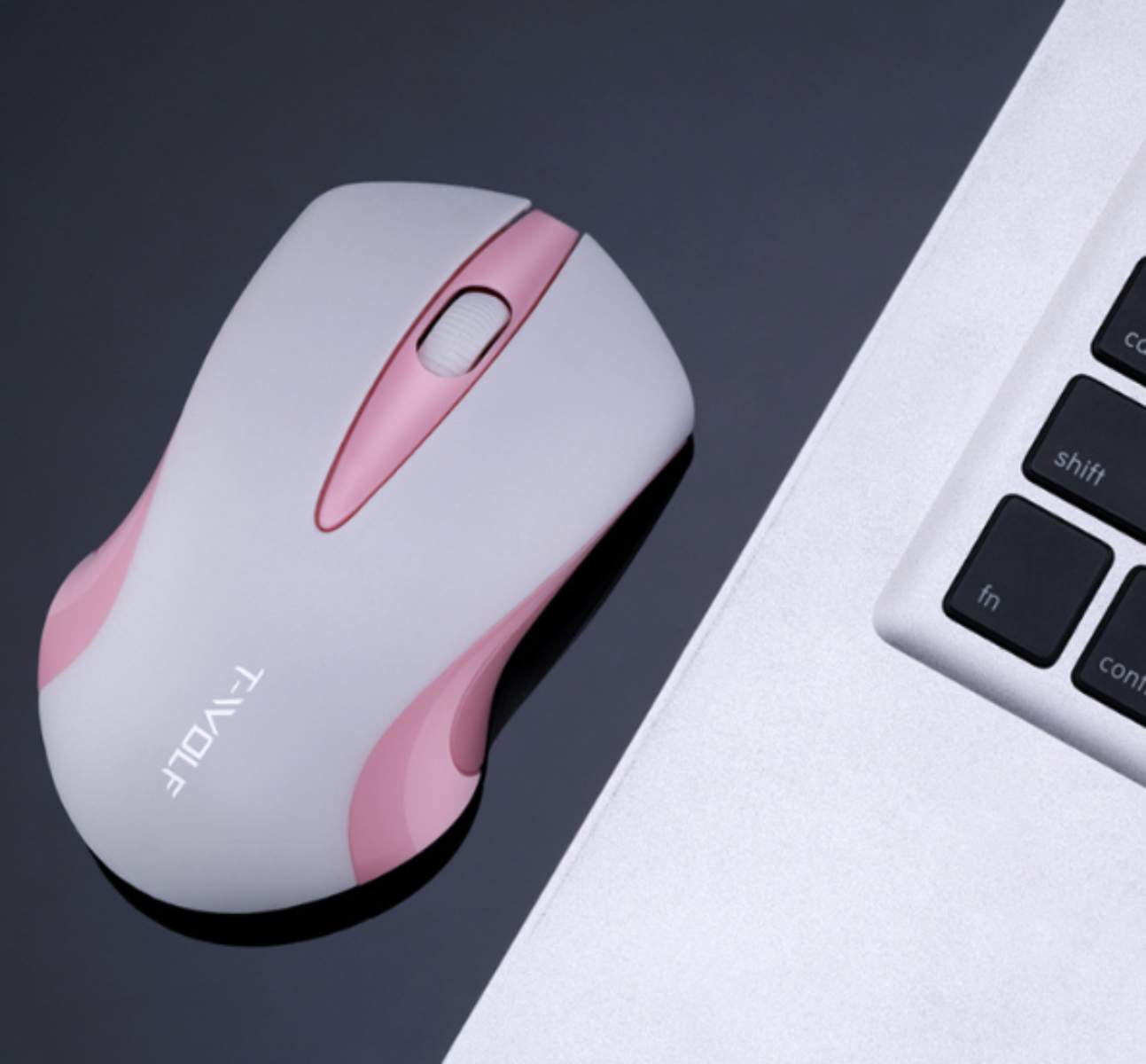 Weiße und rosa Computermaus auf schwarzer Oberfläche neben Laptop-Tastatur.