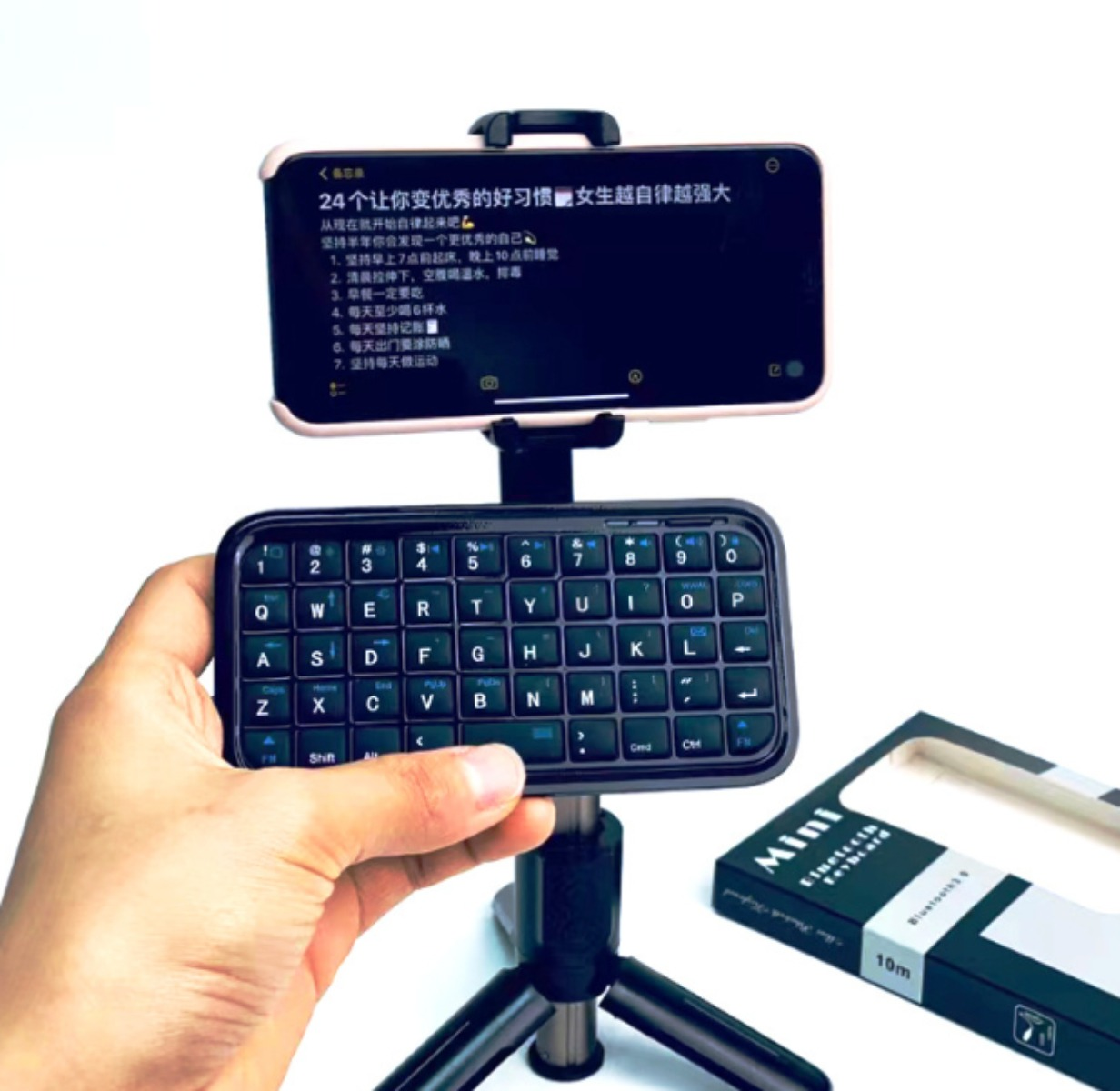 Ein Telefon auf einem Ständer mit Mini-Tastatur davor, von einer Hand gehalten, mit Box.