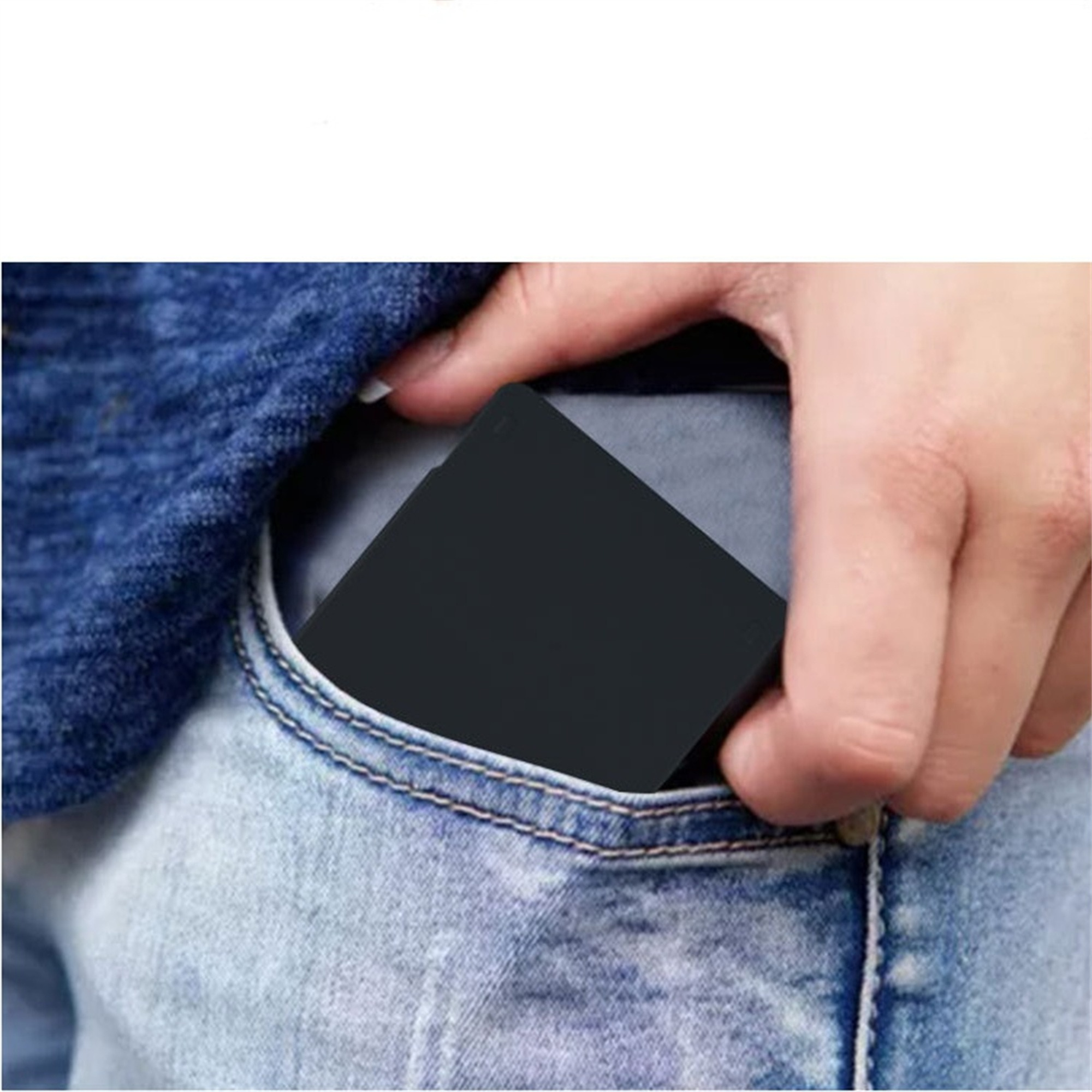 Hand hält ein kleines schwarzes quadratisches Objekt in einer Jeans-Tasche. Das Objekt ist flach.