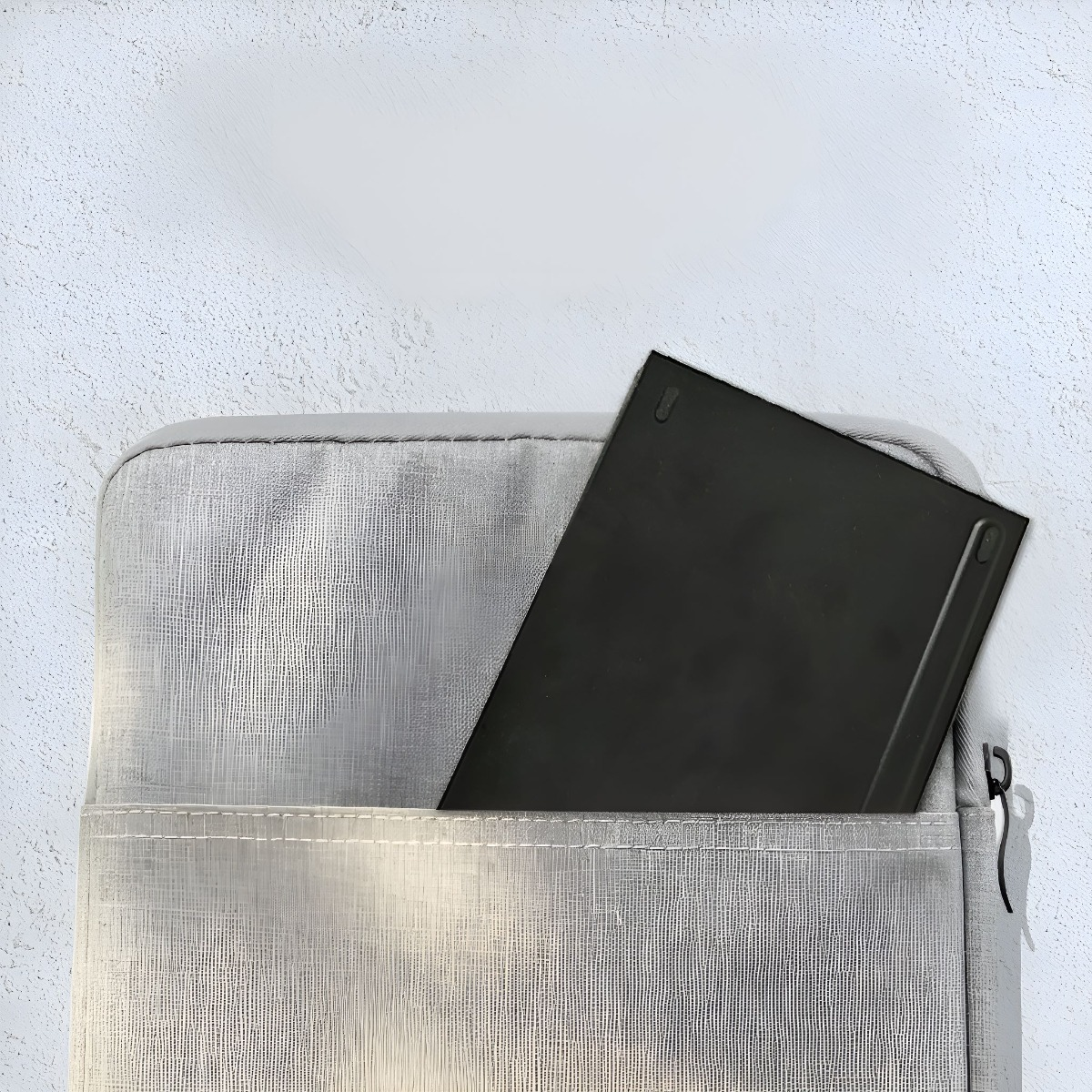 Eine silberne Tasche mit einem schwarzen Objekt darin. Die Tasche befindet sich auf einer weißen und hellgrauen Oberfläche.