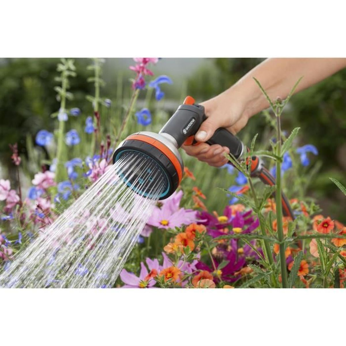 Una persona innaffia i fiori con un tubo da giardino. L'acqua esce dallo spruzzatore.
