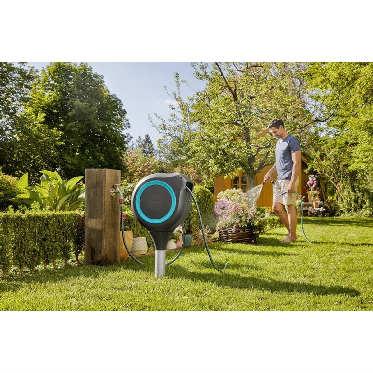 Uomo che innaffia le piante con un tubo in giardino. Erba verde e alberi sullo sfondo.