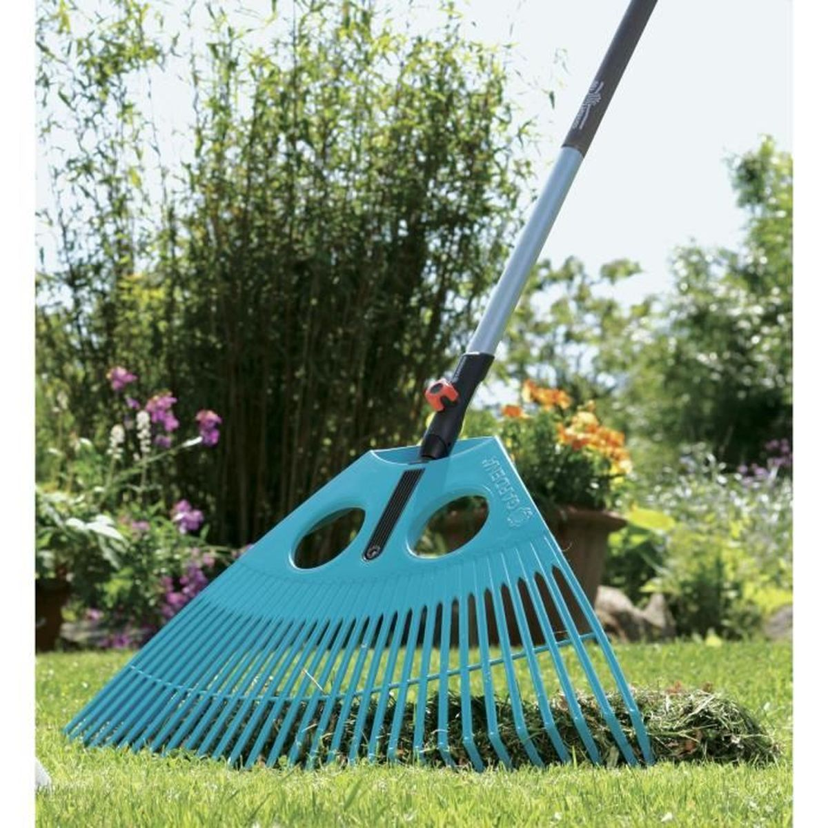 Un rastrello blu giace sull'erba verde con uno sfondo sfocato di cespugli e fiori.