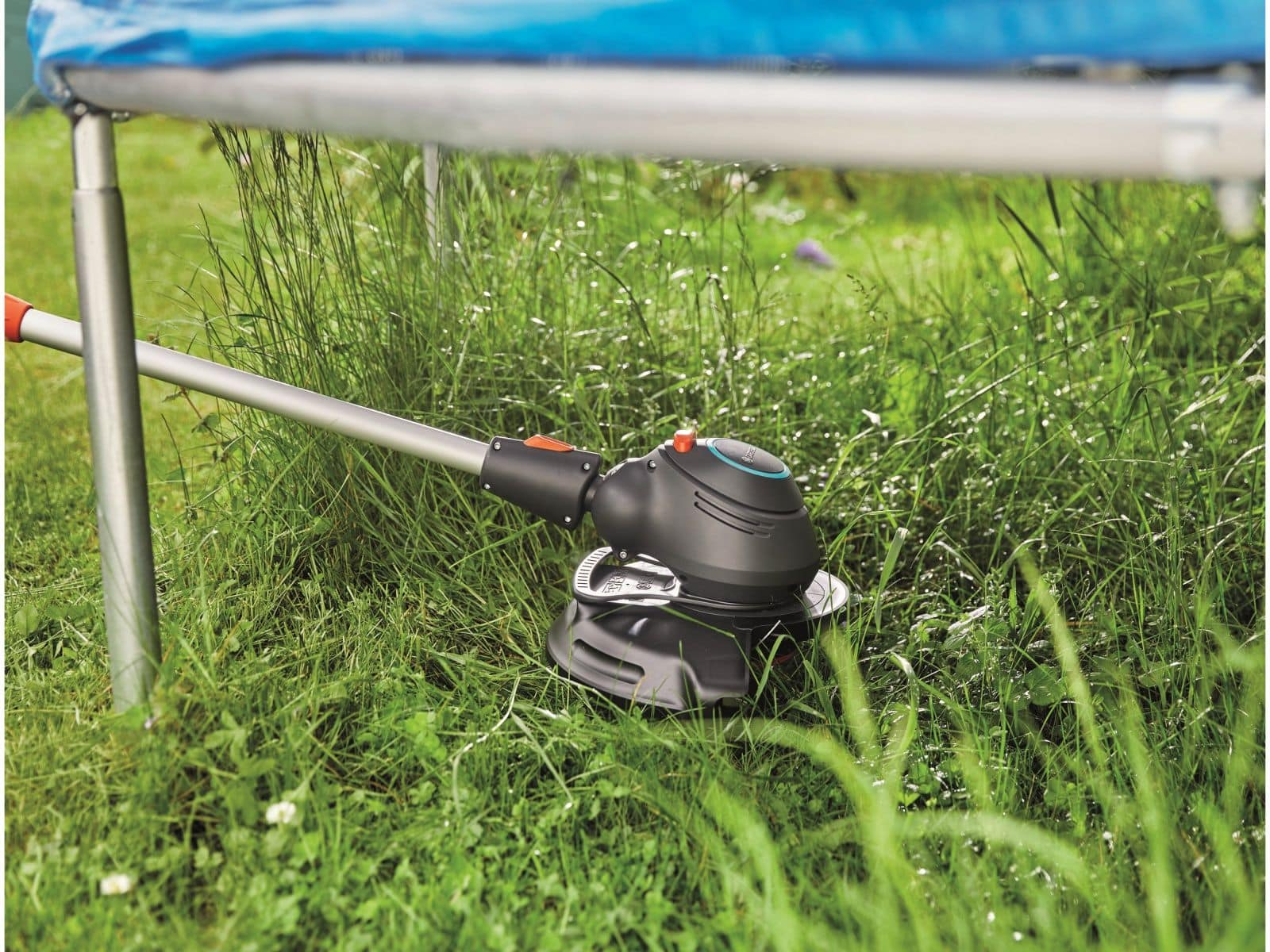 Ein schwarz-grauer Rasentrimmer liegt auf grünem Gras, darüber ein Trampolin.