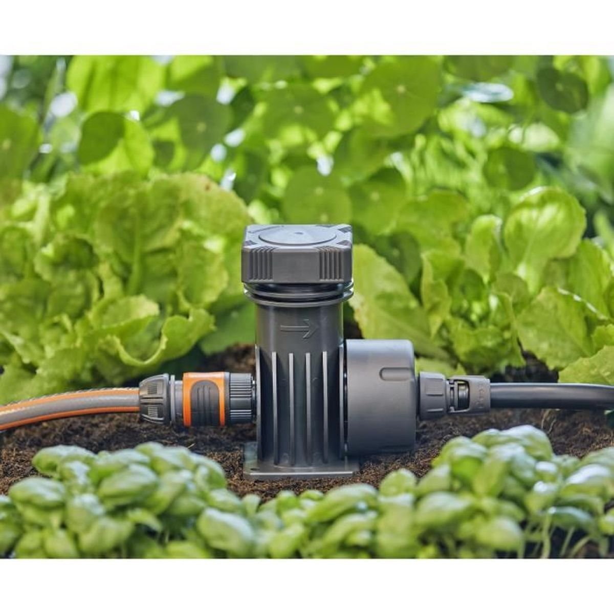 Ein Gartenbewässerungssystem mit schwarzer Steuereinheit und Verbindungsschläuchen, vor grünen Pflanzen.