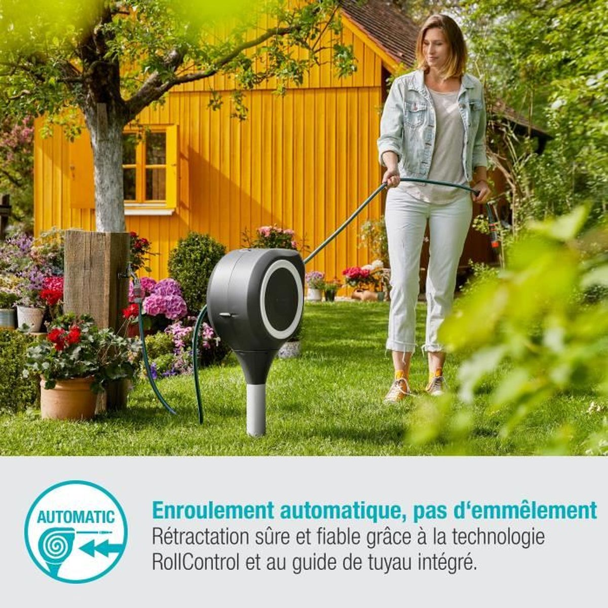 Eine Frau in weißer Hose benutzt eine Schlauchtrommel in einem grünen Garten mit einem gelben Haus im Hintergrund.