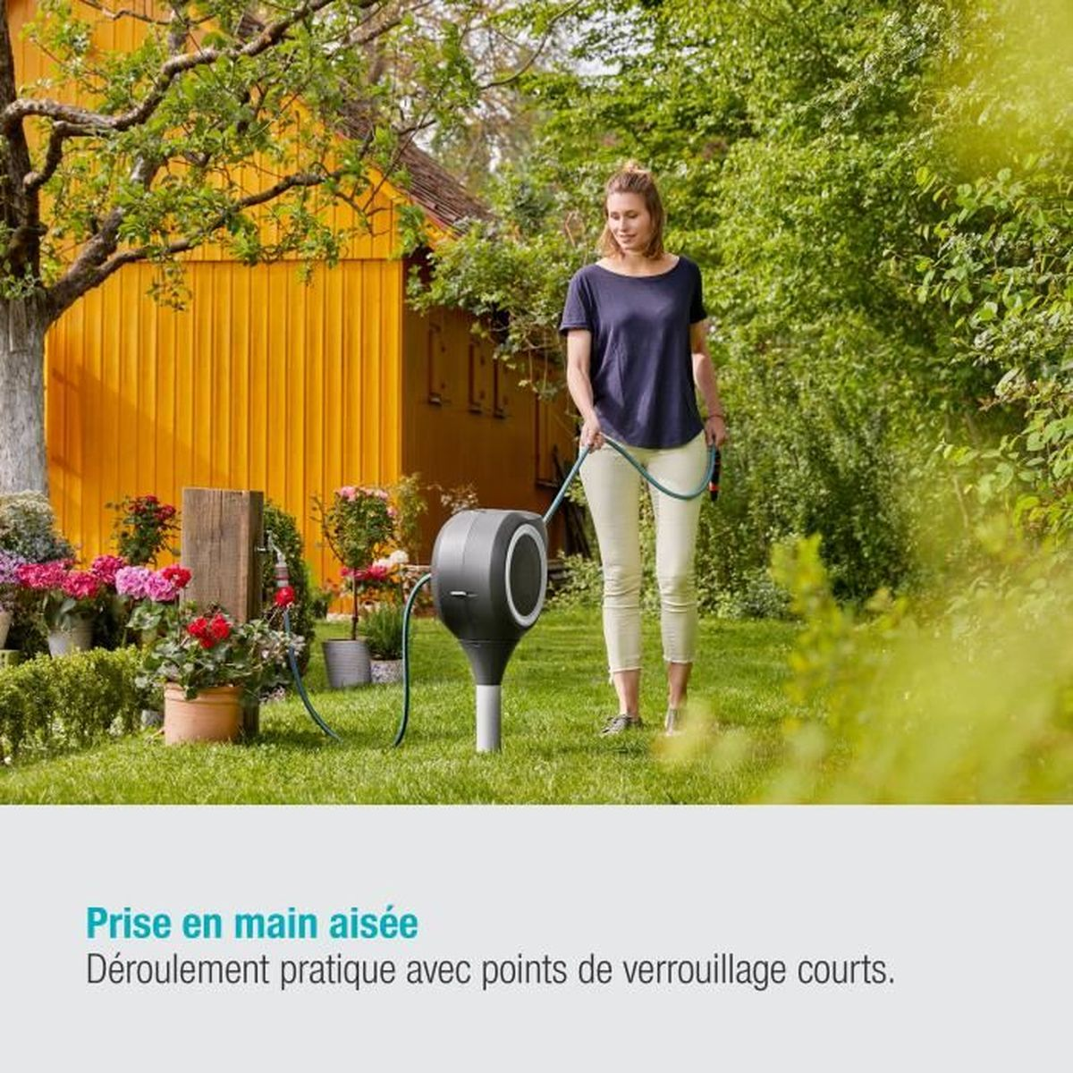 Eine Frau gießt Pflanzen mit einem Schlauch im Garten. Eine Schlauchtrommel ist in der Nähe.