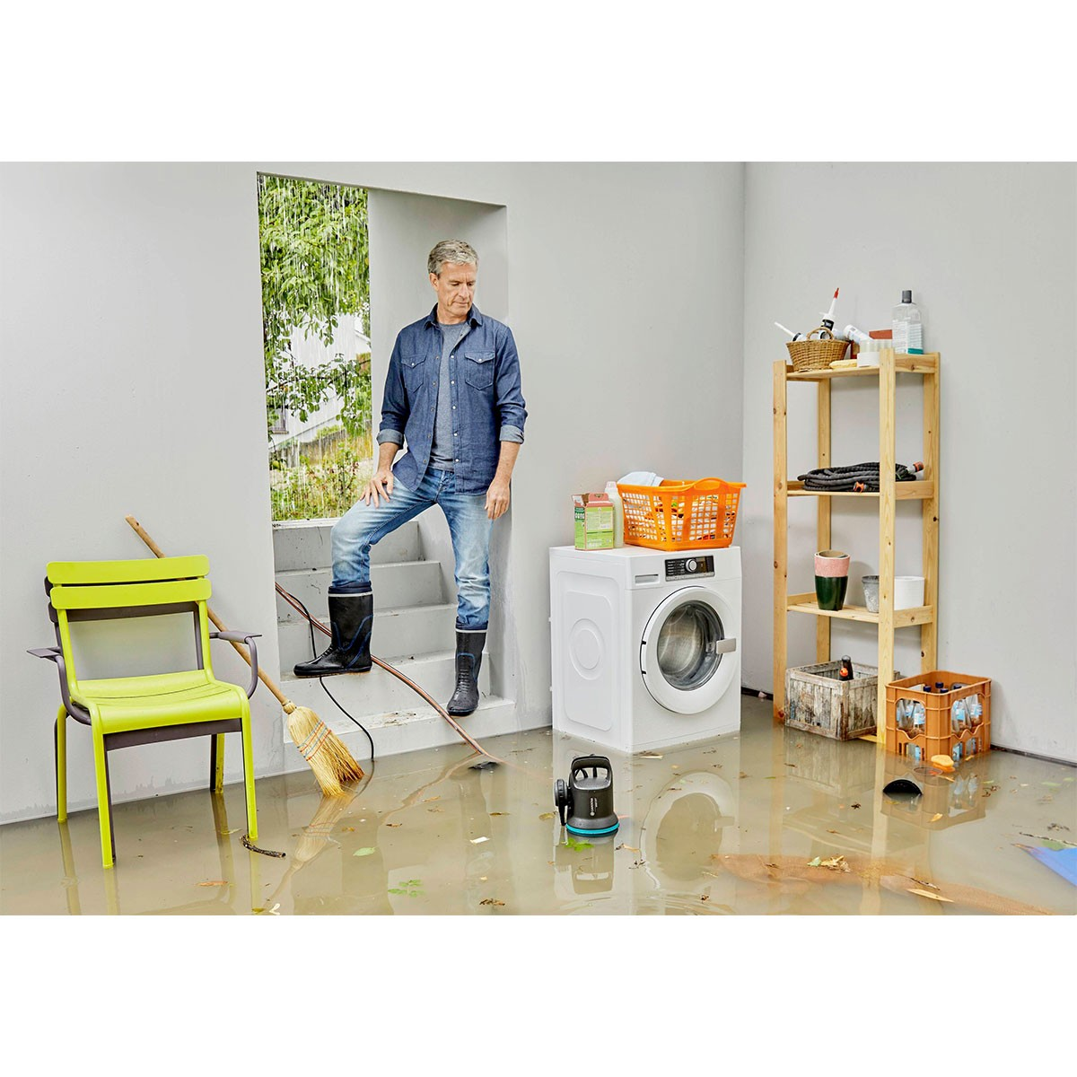 Mężczyzna w zalanej wodą pokoju stoi w drzwiach. Pralka, krzesło i półka są w wodzie.