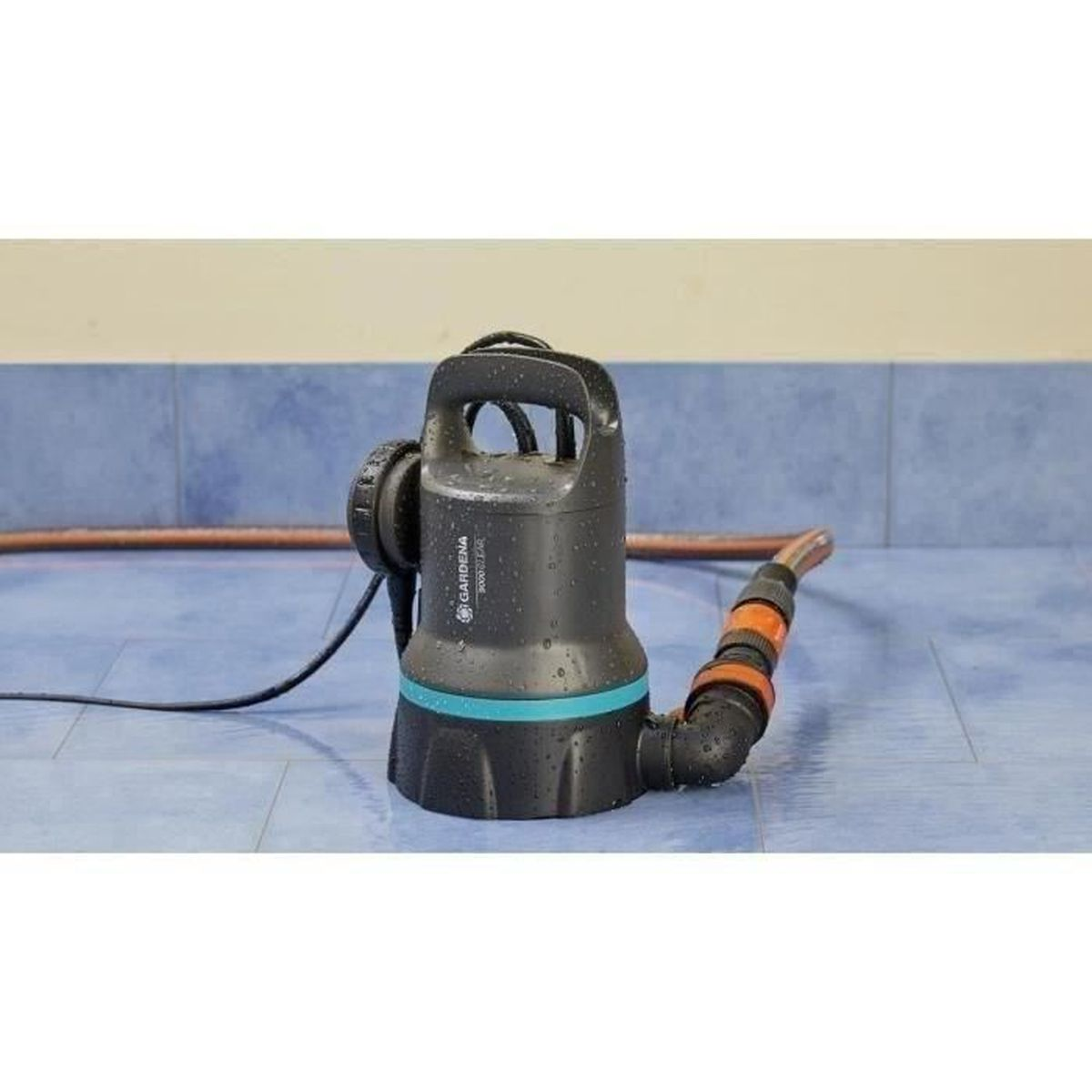 Pompa sommersa nera su pavimento piastrellato blu, con tubo e testo.
