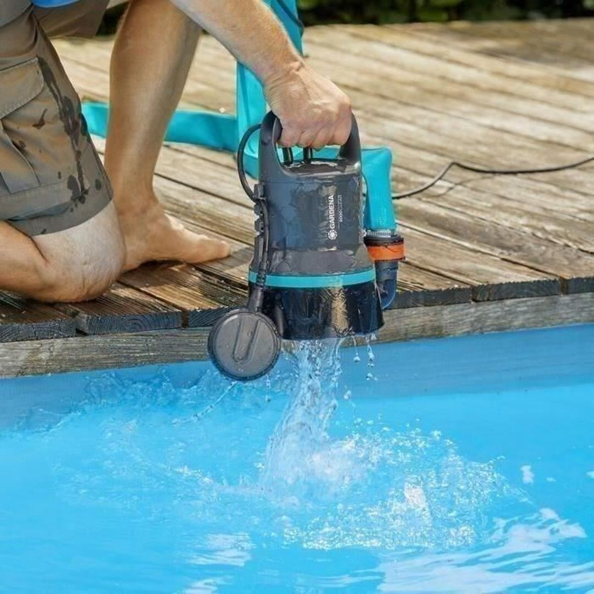 Una persona che tiene una pompa dell'acqua nera e verde acqua, pompando acqua in una piscina blu.