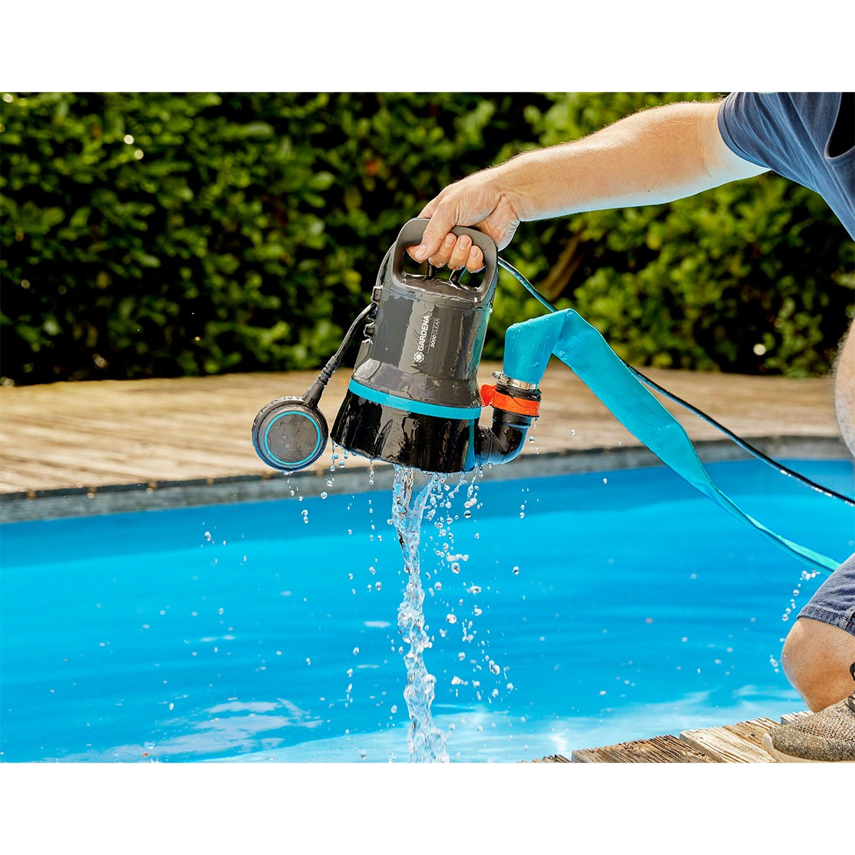 Una persona pompa acqua da una piscina. Una pompa nera è in acqua, collegata a un tubo.