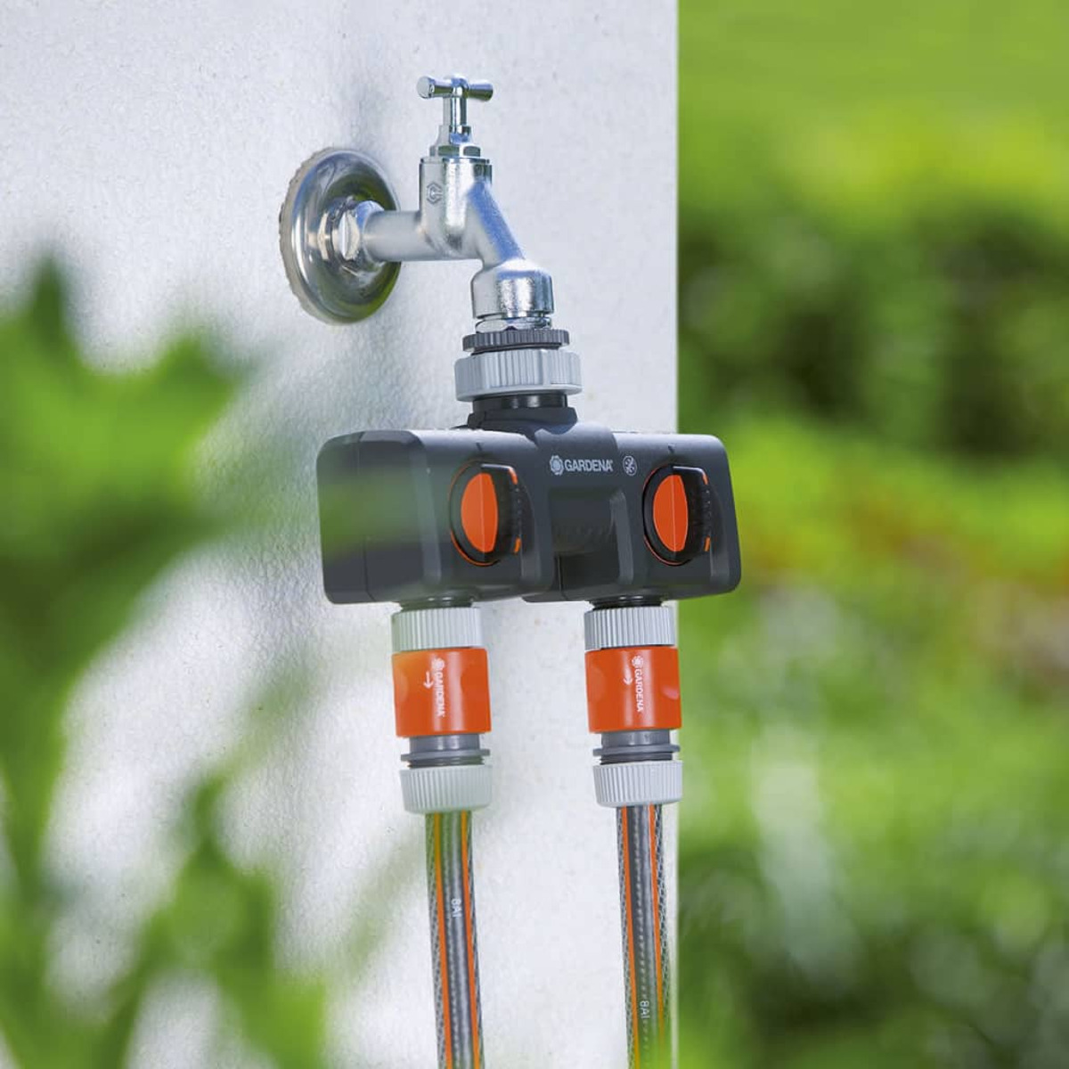 Wasserhahn mit einem schwarzen Zweiwege-Anschluss. Orange und graue Schläuche sind angeschlossen.
