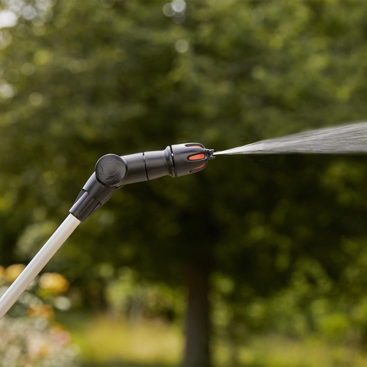 Ein schwarzes und silbernes Sprühgerät sprüht Wasser, mit verschwommenem grünem Hintergrund.