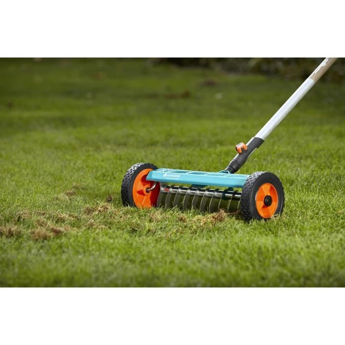Lawn aerator with orange wheels is on green grass, some dead grass is beside it.
