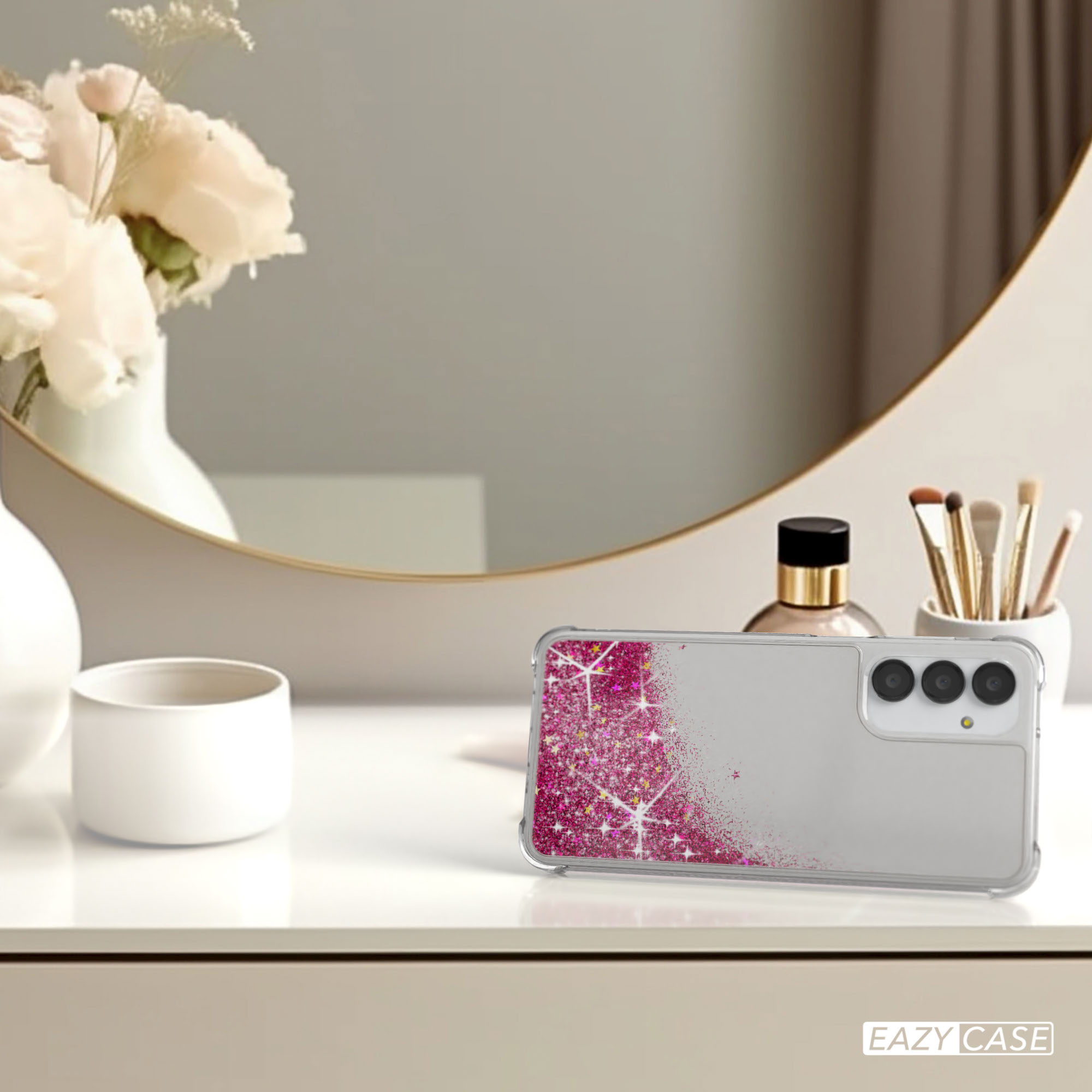 Eine Handyhülle mit pinkfarbenem Glitzerdesign auf einem Tisch mit Spiegel und Make-up.