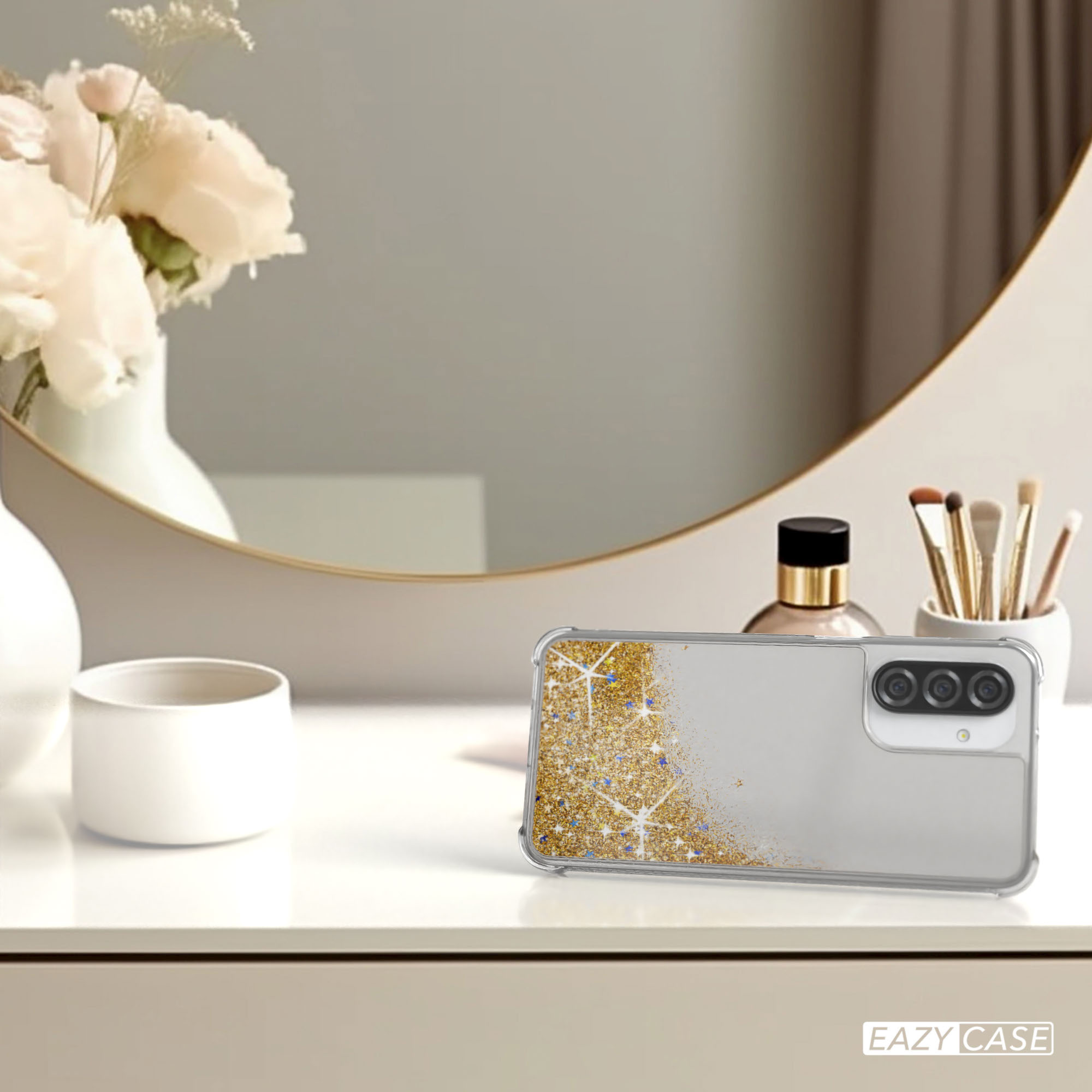 Handyhülle mit goldenem Glitzerdesign auf einem Tisch, in der Nähe eines Spiegels, Parfums und Make-up-Pinseln.