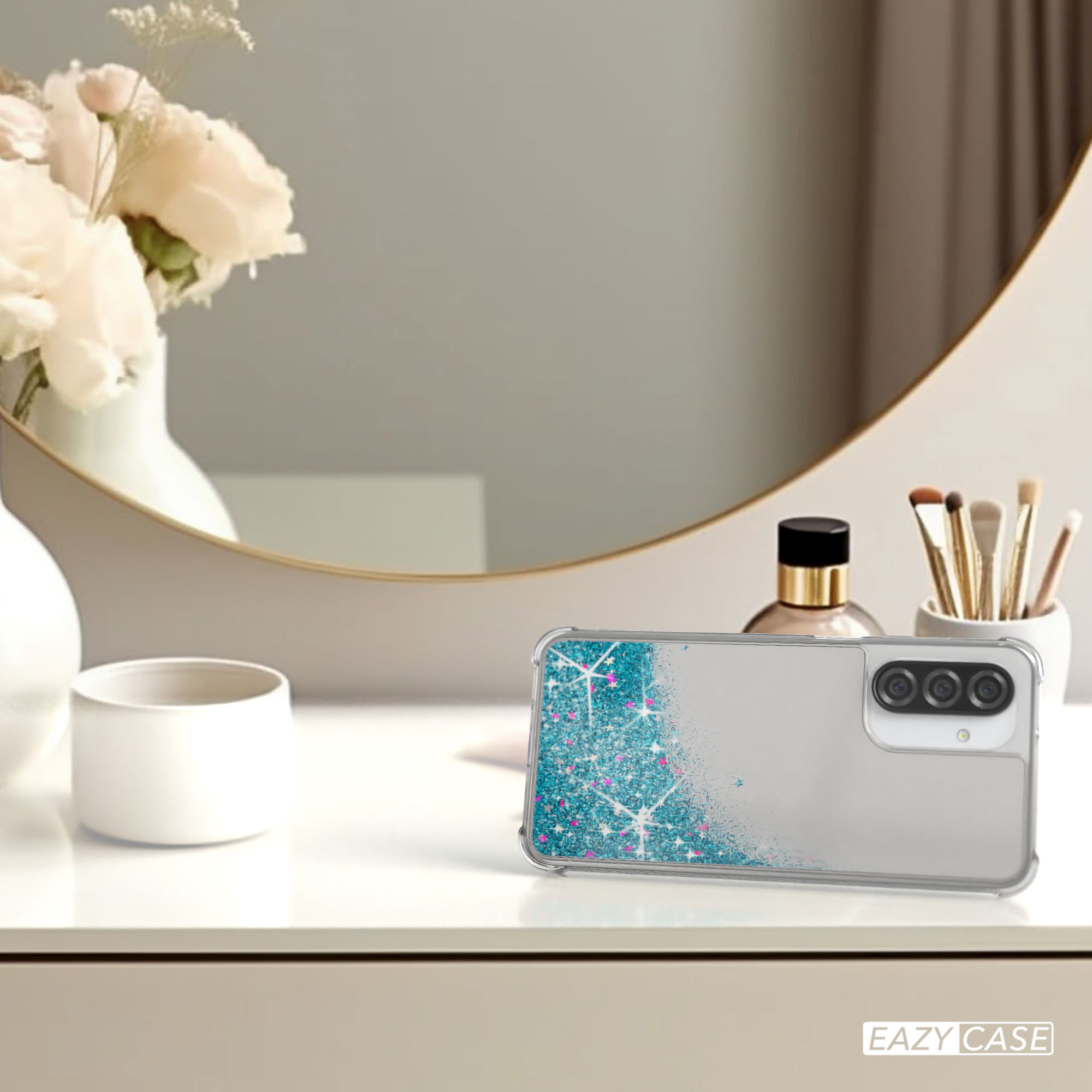 Handyhülle mit Glitzer auf Tisch, neben Spiegel, Blumen und Make-up.