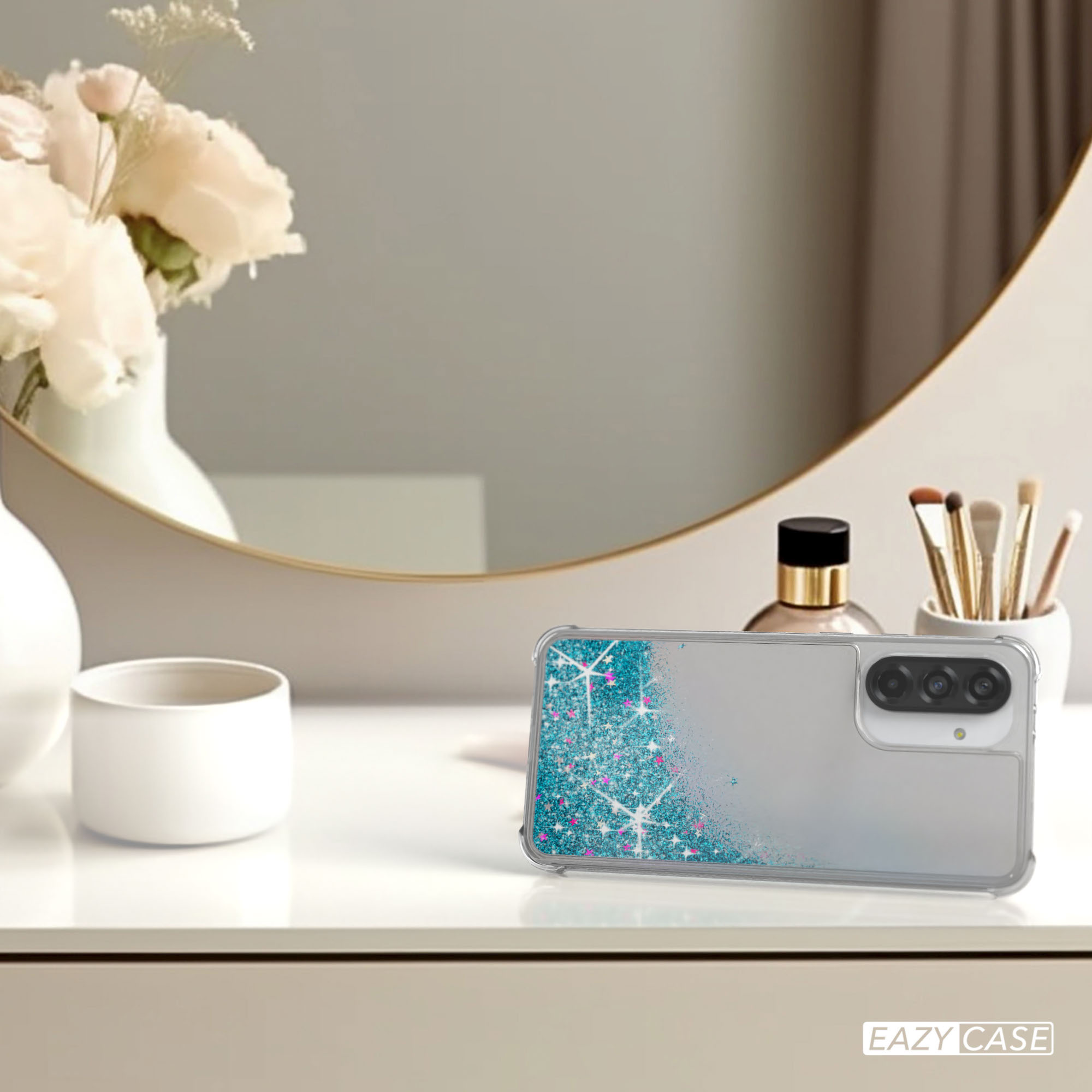 Eine Handyhülle mit Flüssigkeitsglitzer-Design. Ein Spiegel, Parfüm und Make-up-Pinsel sind im Hintergrund.