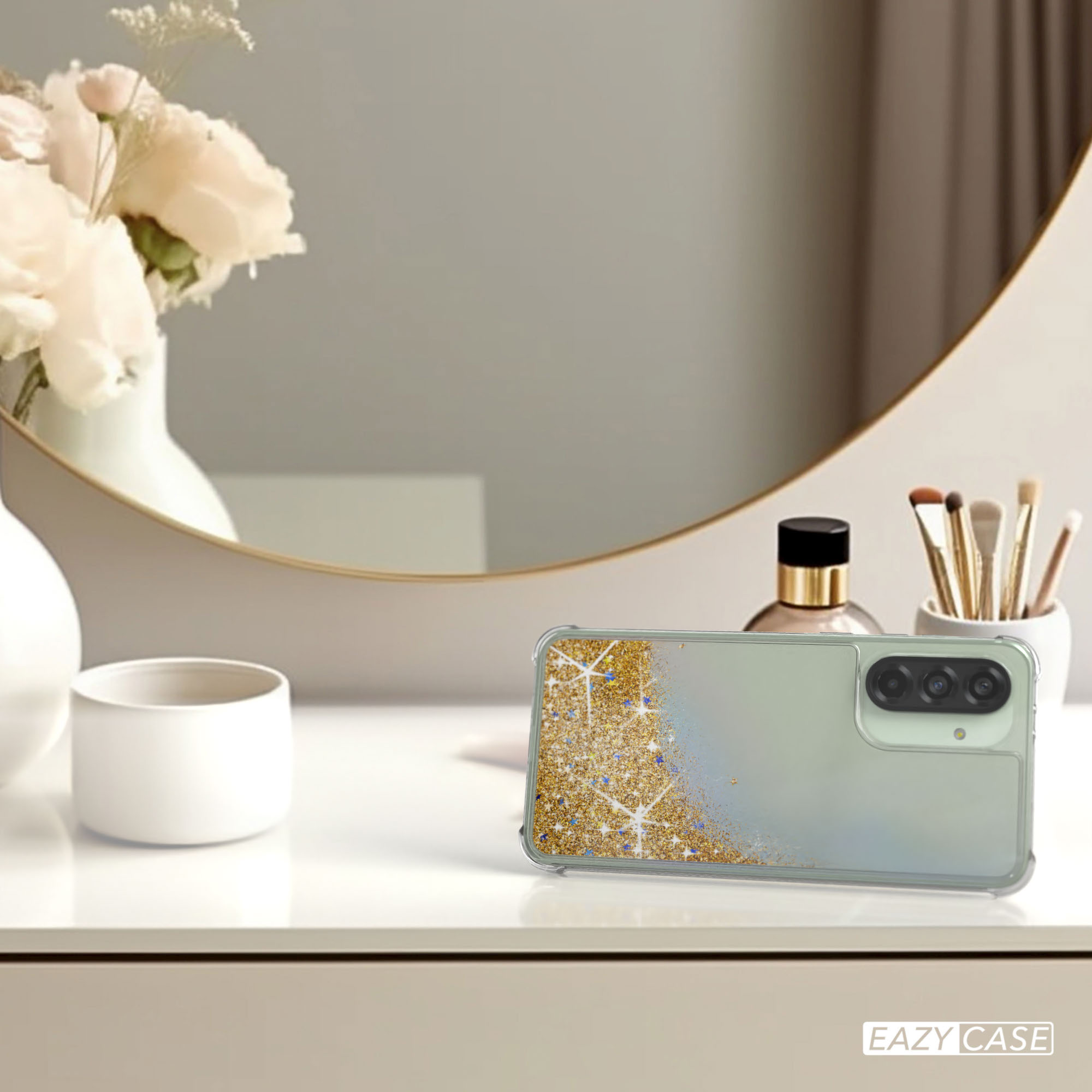 Handyhülle mit goldenem Glitzer, andere Objekte auf einem Tisch neben einem Spiegel.