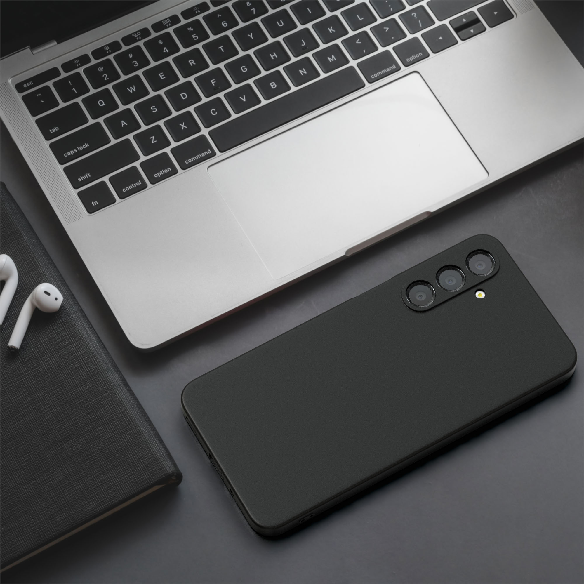 Schwarzes Smartphone auf dunkler Oberfläche mit Laptop, Kopfhörern und Notizbuch im Blick.
