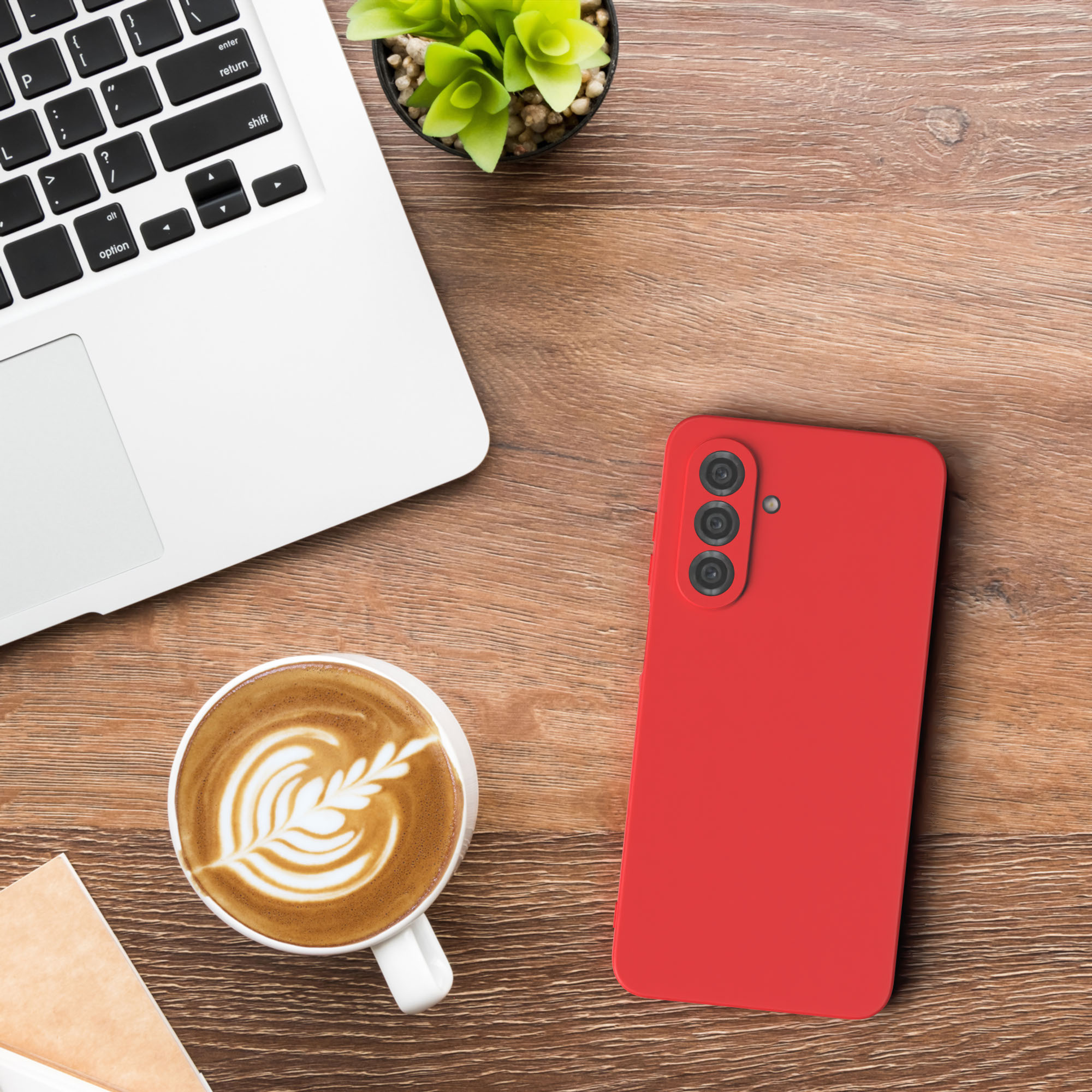 Ein Laptop, ein rotes Telefon, eine Tasse Kaffee und eine Pflanze auf einem Holztisch.