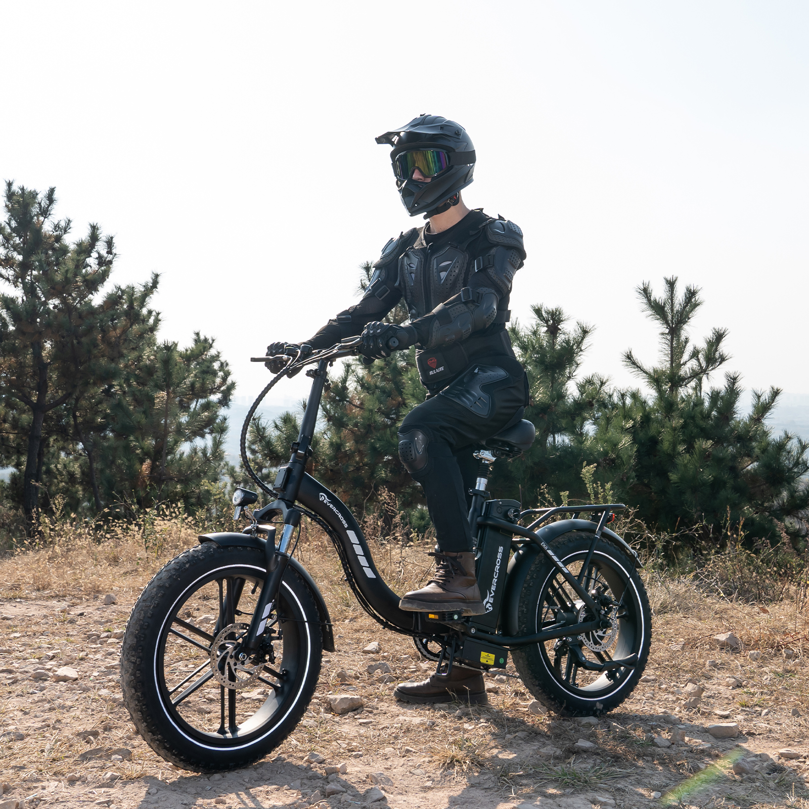 Persoon in beschermende kleding rijdt op een zwarte elektrische fiets op een zandpad. De fiets heeft dikke banden.