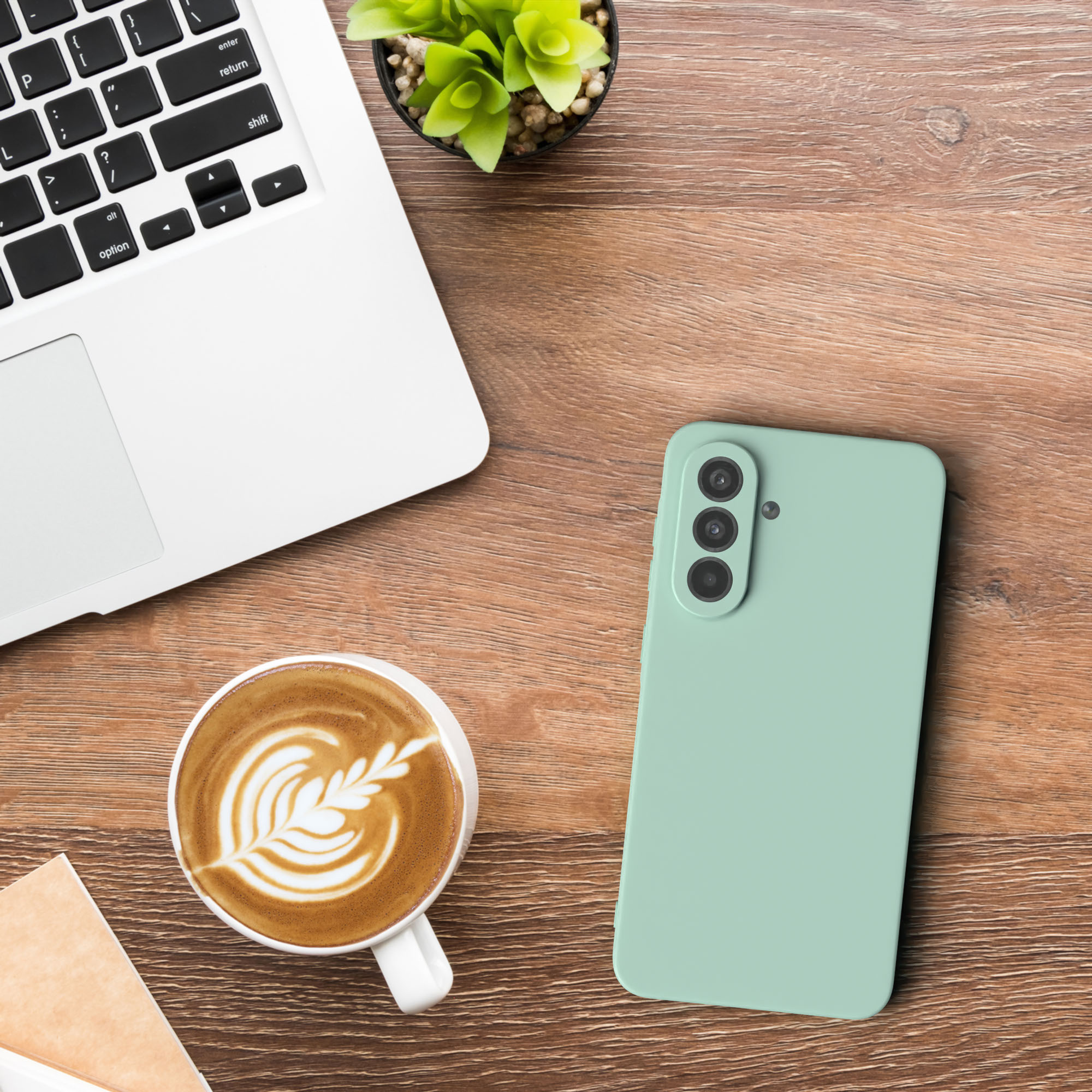 Ein Laptop, Kaffee mit Latte Art, ein Telefon und eine Pflanze auf einem Holzschreibtisch.