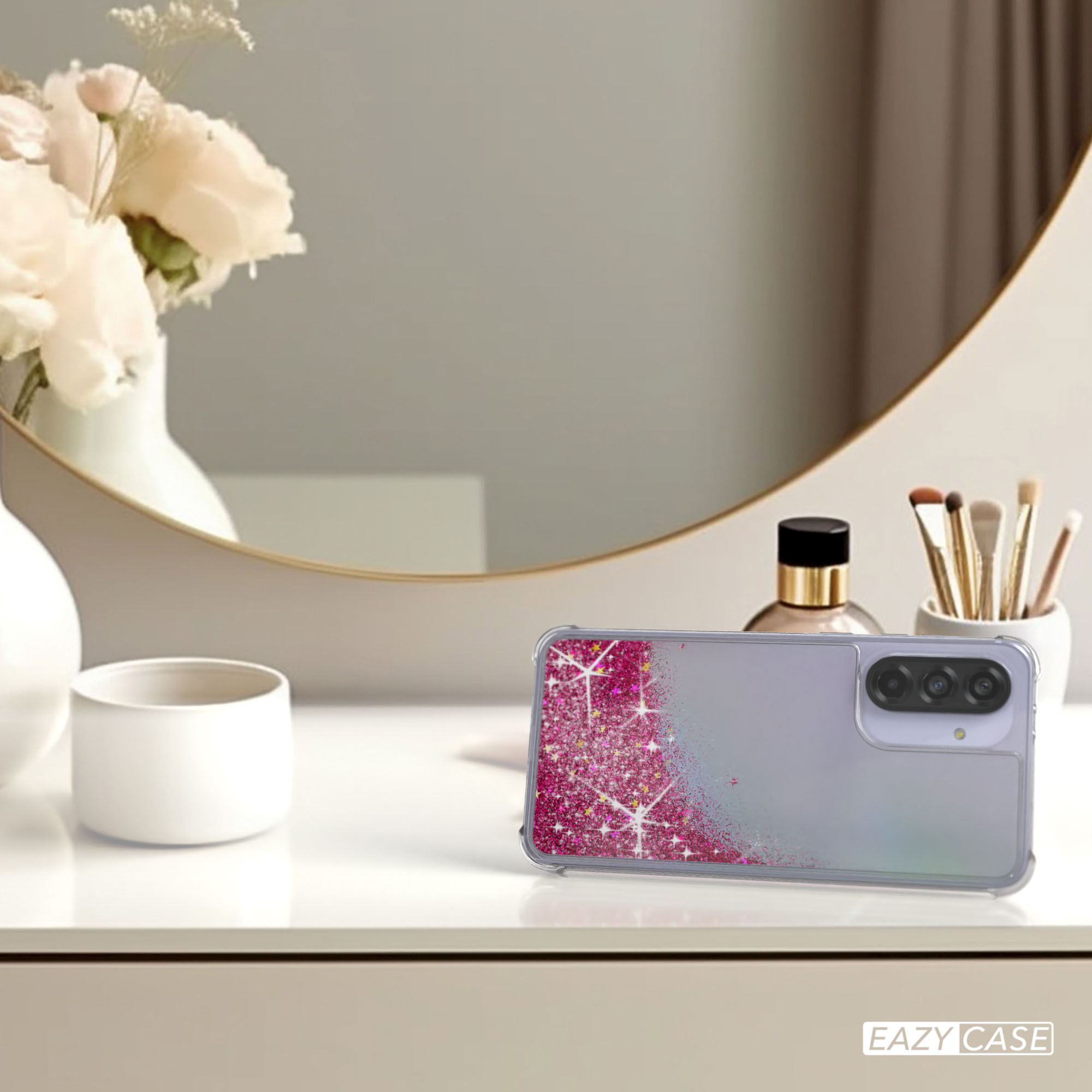Handyhülle mit Glitzer und Blumen auf einem Tisch. Spiegel und Vase im Hintergrund.
