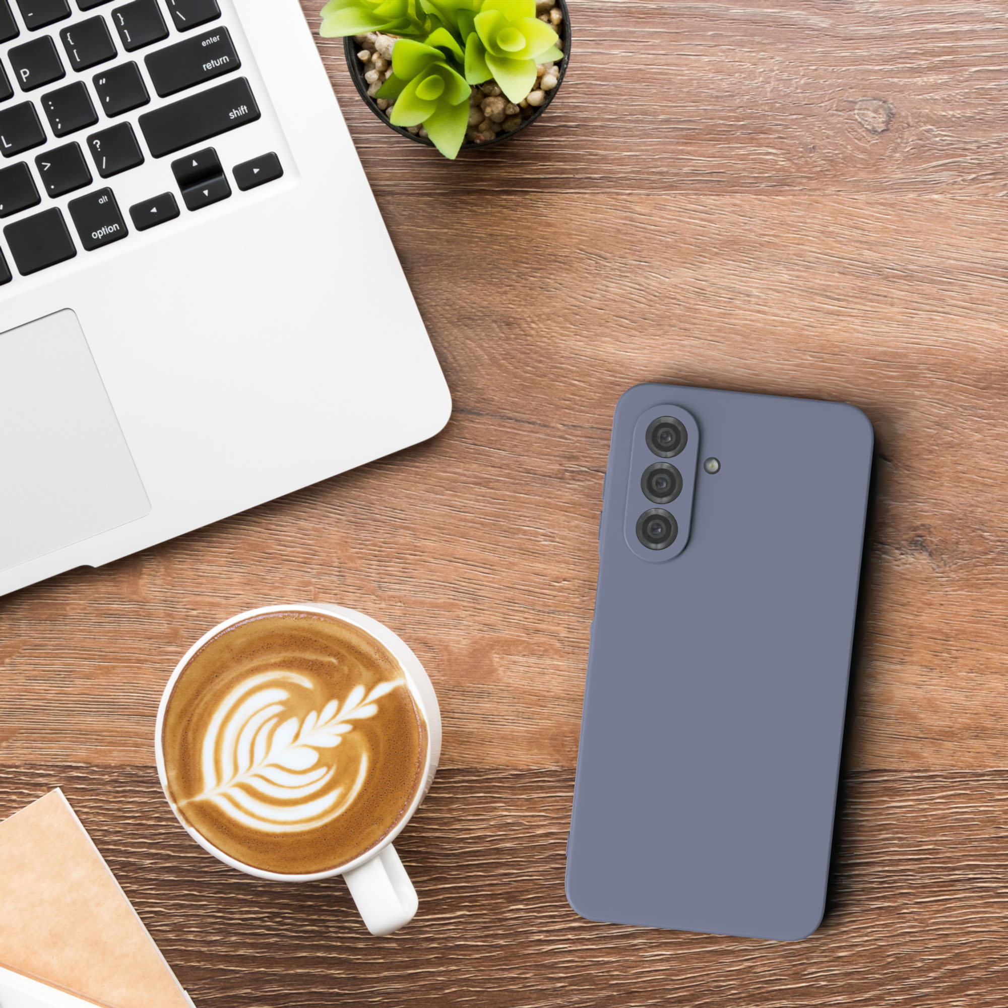 Ein Laptop, eine Kaffeetasse, ein Telefon und eine Pflanze auf einem Holzschreibtisch.