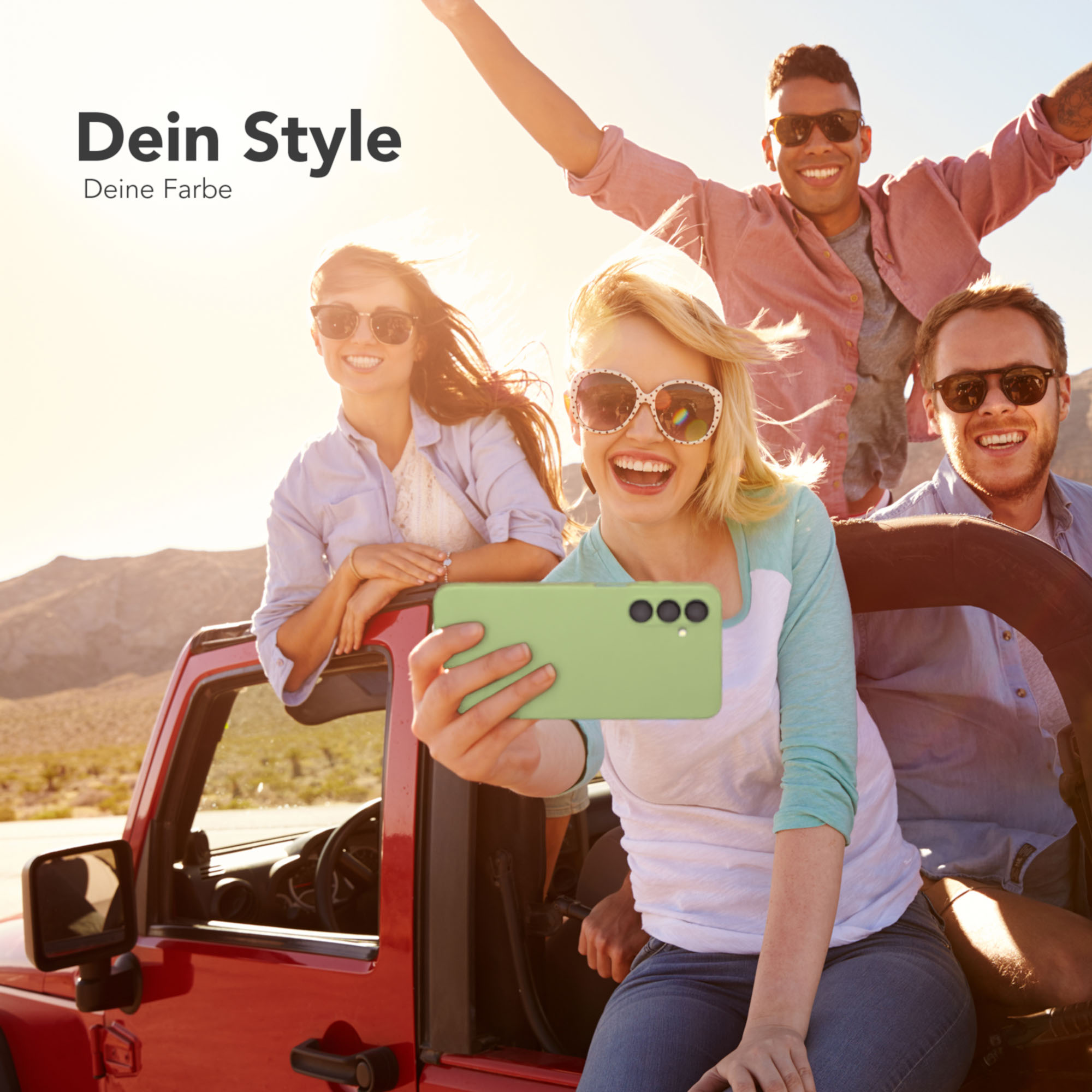 Vier Freunde in einem roten Jeep machen ein Selfie. Einer hält ein grünes Handy. Lächeln.