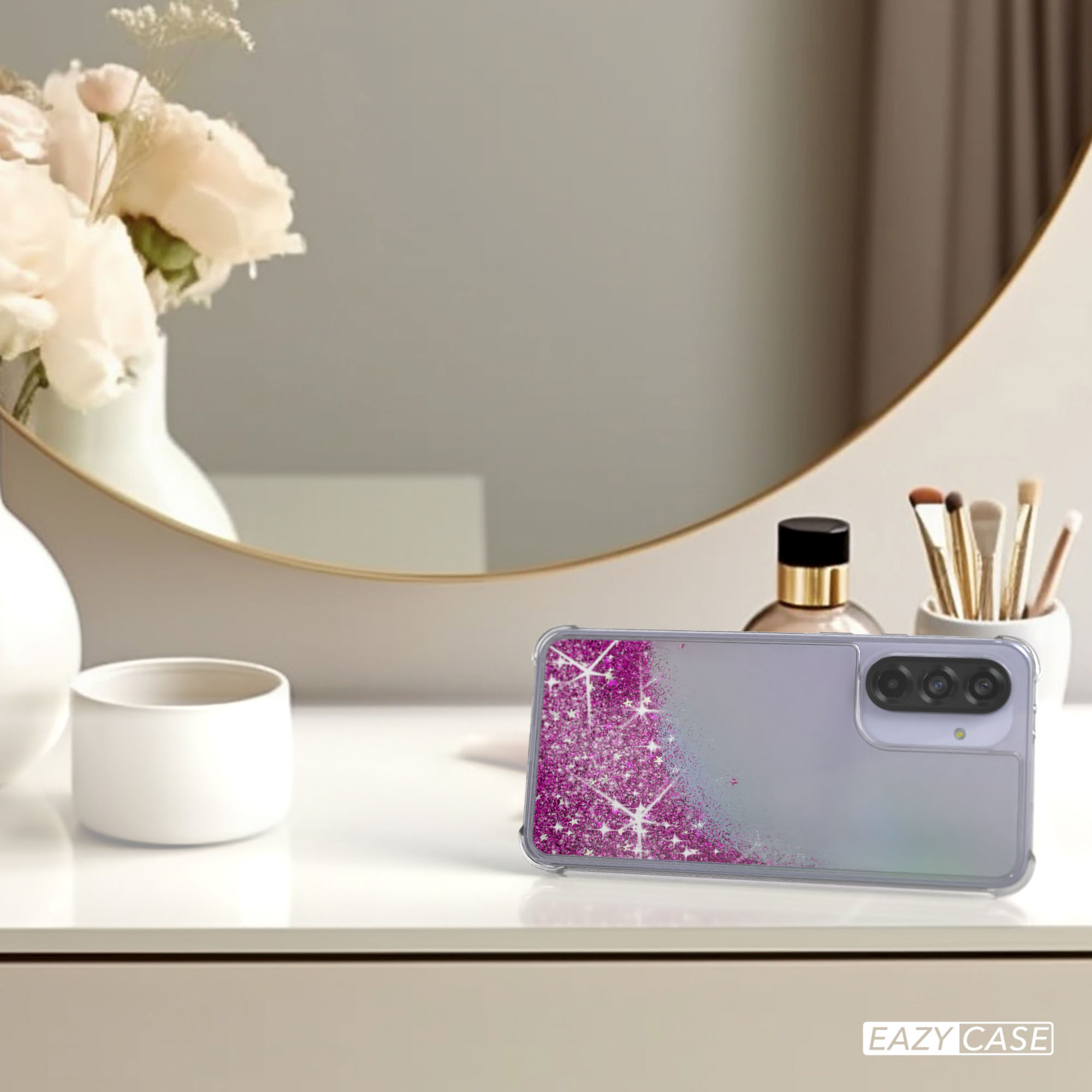 Eine Handyhülle mit Glitzerdesign liegt auf einem Tisch mit Spiegel und Blumen.