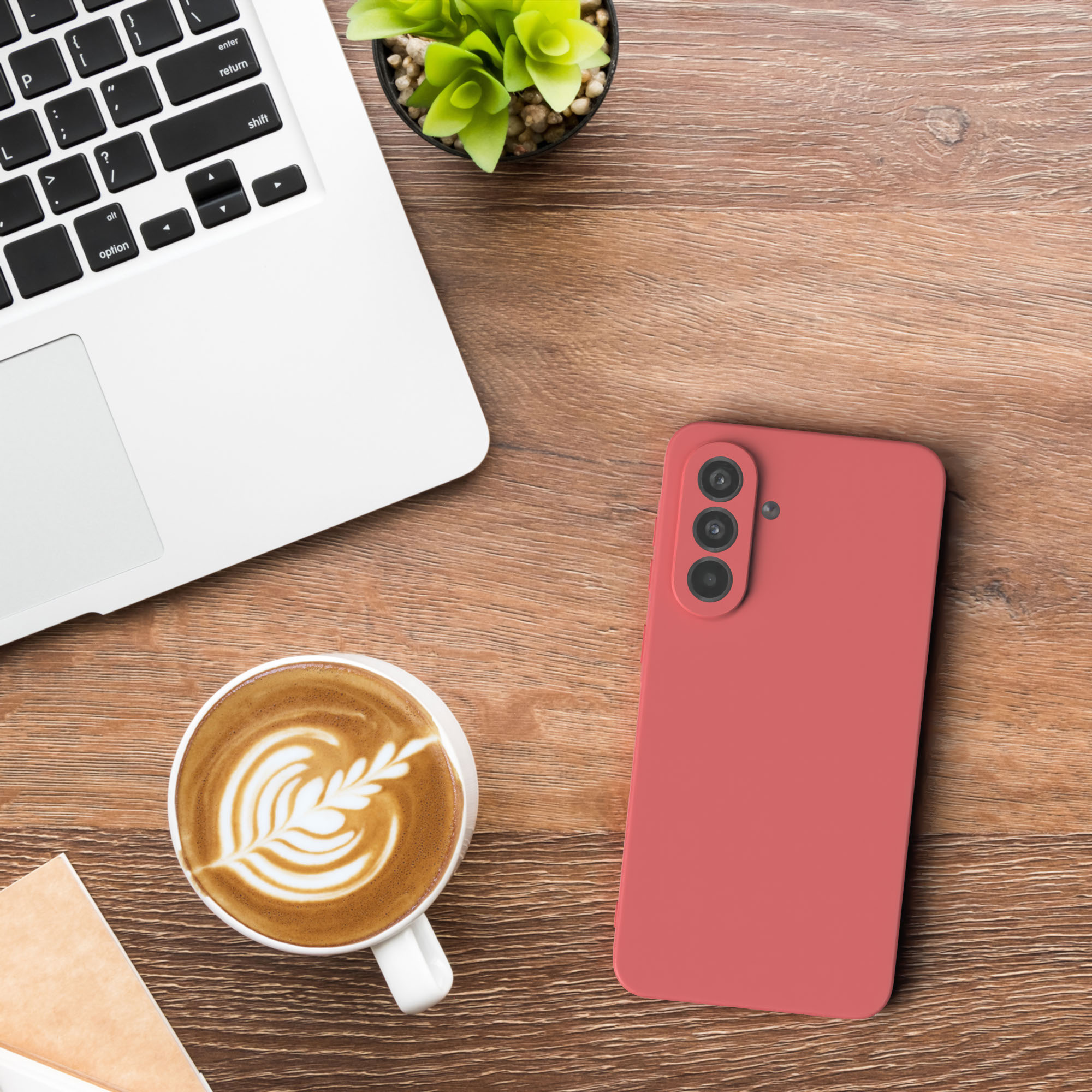 Ein Laptop, ein rosa Telefon und eine Kaffeetasse mit Latte Art stehen auf einem Holztisch.
