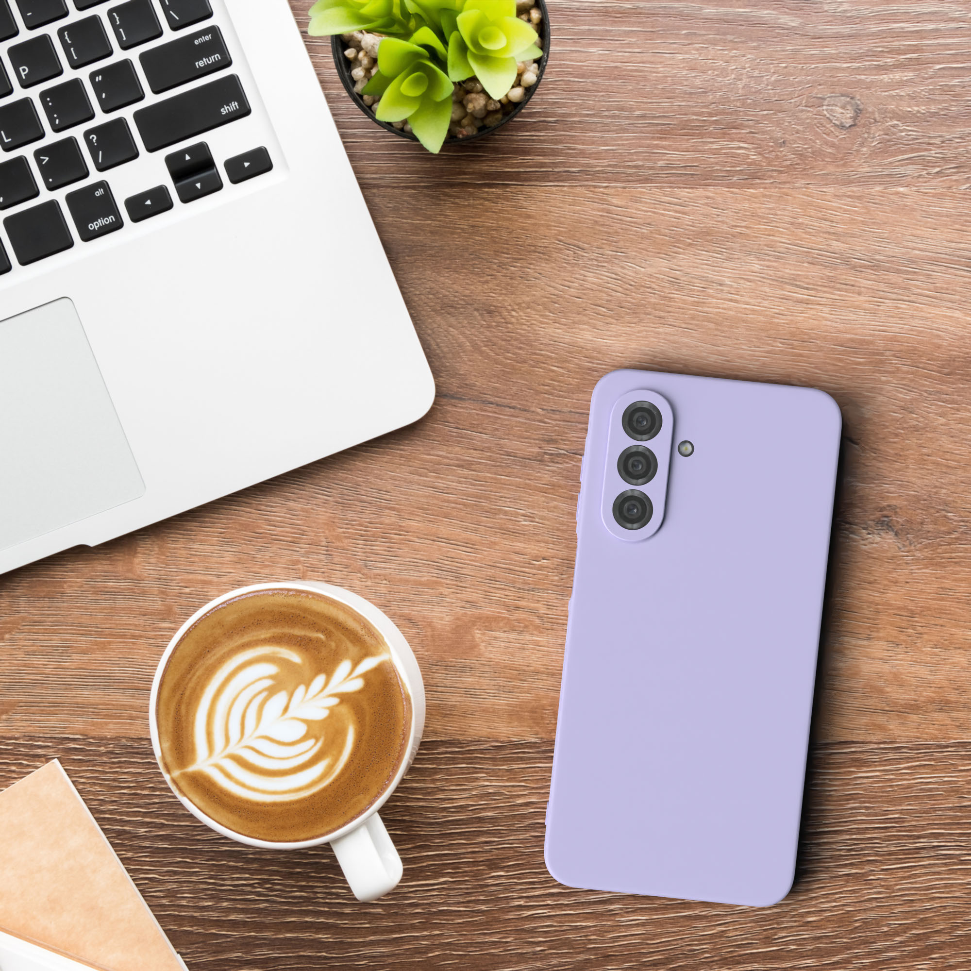 Ein Schreibtisch-Setup mit Laptop, Kaffee, Telefon und einer Pflanze. Das Telefon ist lila.