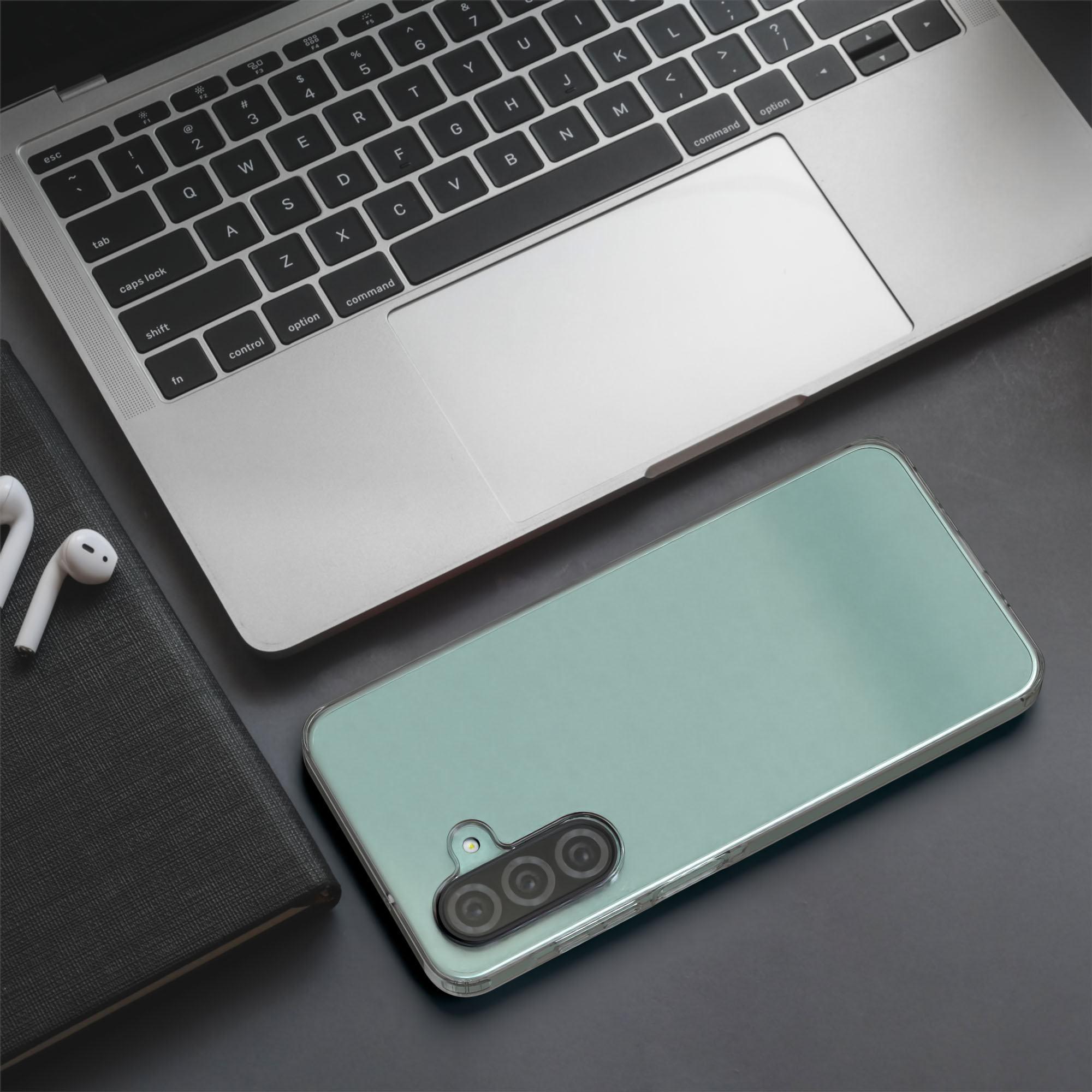 Ein Laptop, Telefon und Kopfhörer liegen auf einer dunklen Oberfläche. Das Telefon hat eine transparente Hülle.
