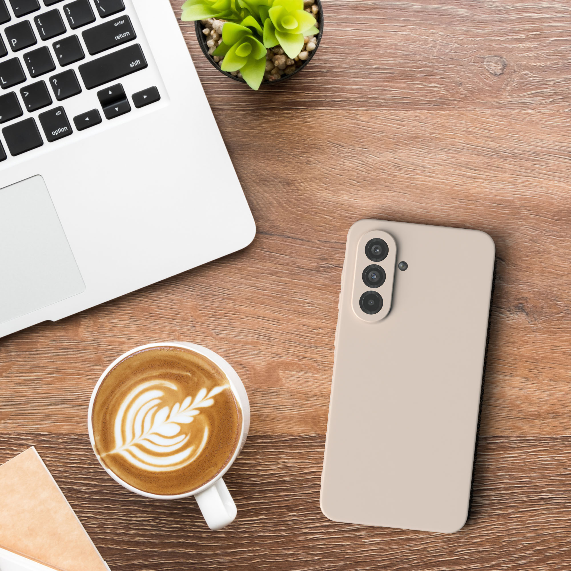 Draufsicht auf einen Schreibtisch mit Laptop, Kaffeetasse mit Latte Art und Telefon in einem beigen Case.