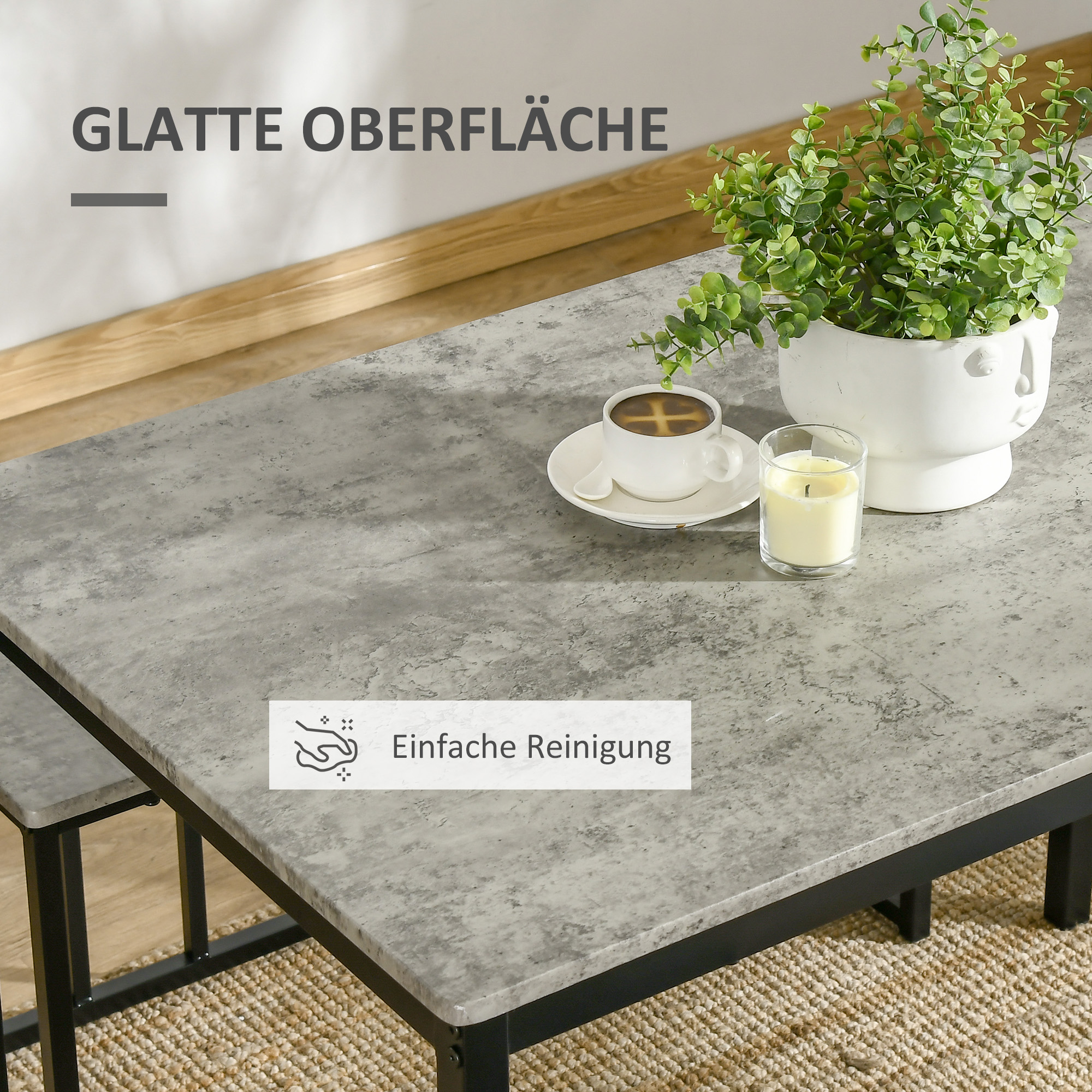 Ein Tisch mit grauer Oberfläche, eine Tasse Kaffee, eine Pflanze und eine Kerze. Der Hintergrund ist ein Teppich.