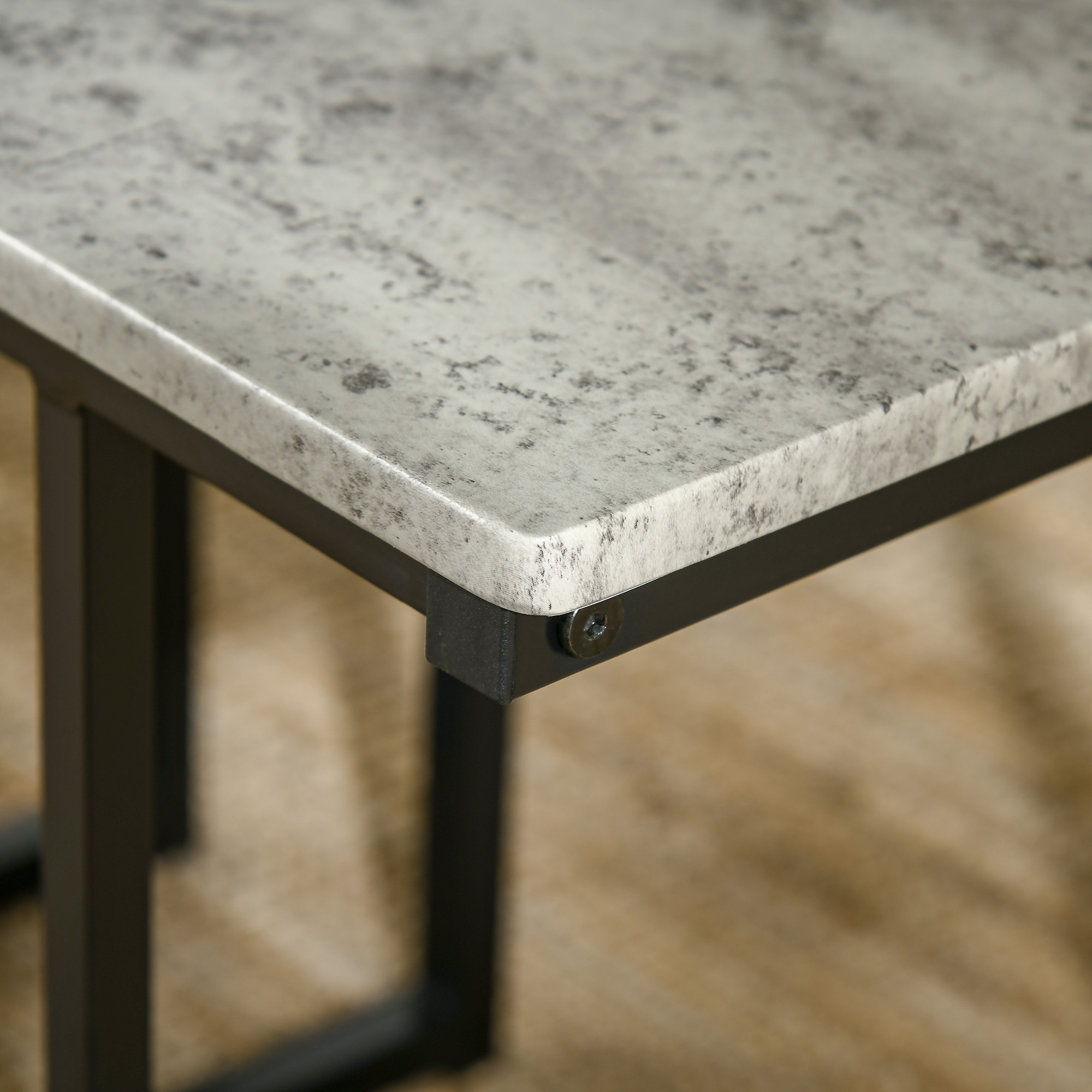 Nahaufnahme einer grauen und schwarzen Tischkante. Der Tisch hat eine gesprenkelte Oberseite und ein schwarzes Metallgestell. Eine Schraube ist sichtbar.