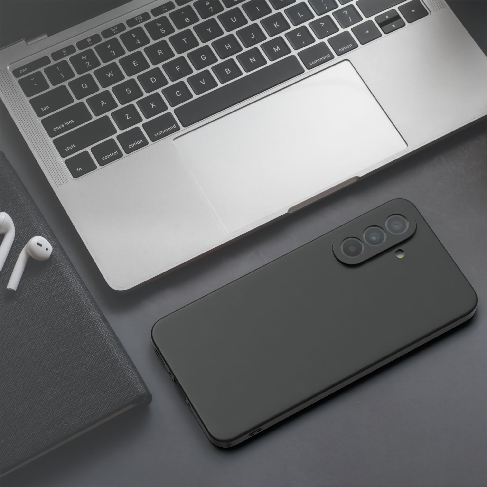 Laptop, Kopfhörer und ein Telefon in einem schwarzen Gehäuse auf dunkler Oberfläche.