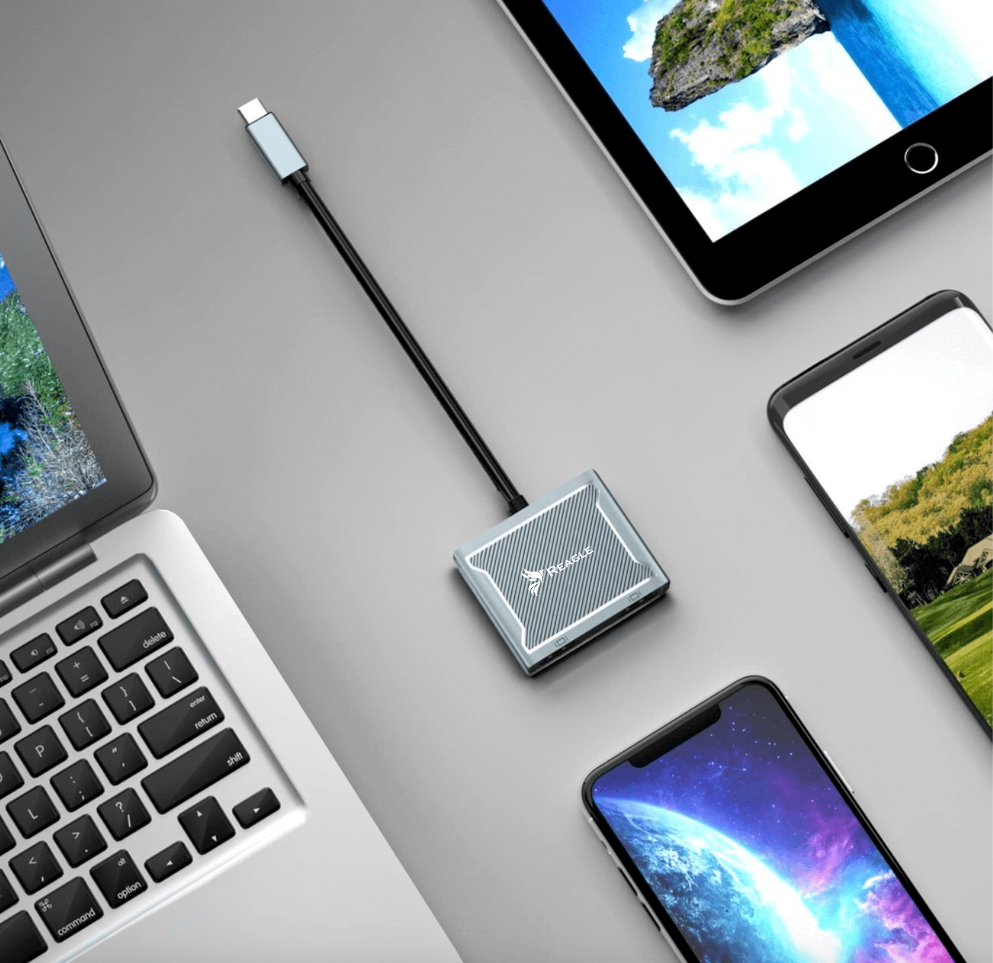 Un laptop, un tablet e due smartphone collegati a un adattatore argentato. Sfondo di superficie grigia.
