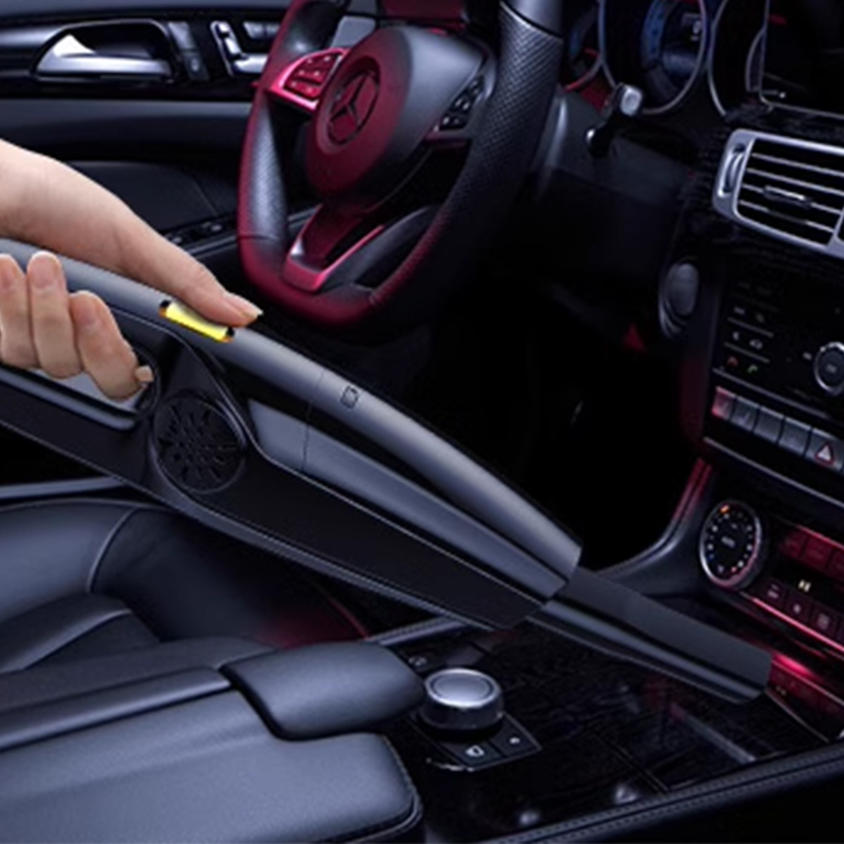 Eine Hand drückt eine Taste an einem schwarzen Staubsauger für Autos, im Inneren eines Autos.