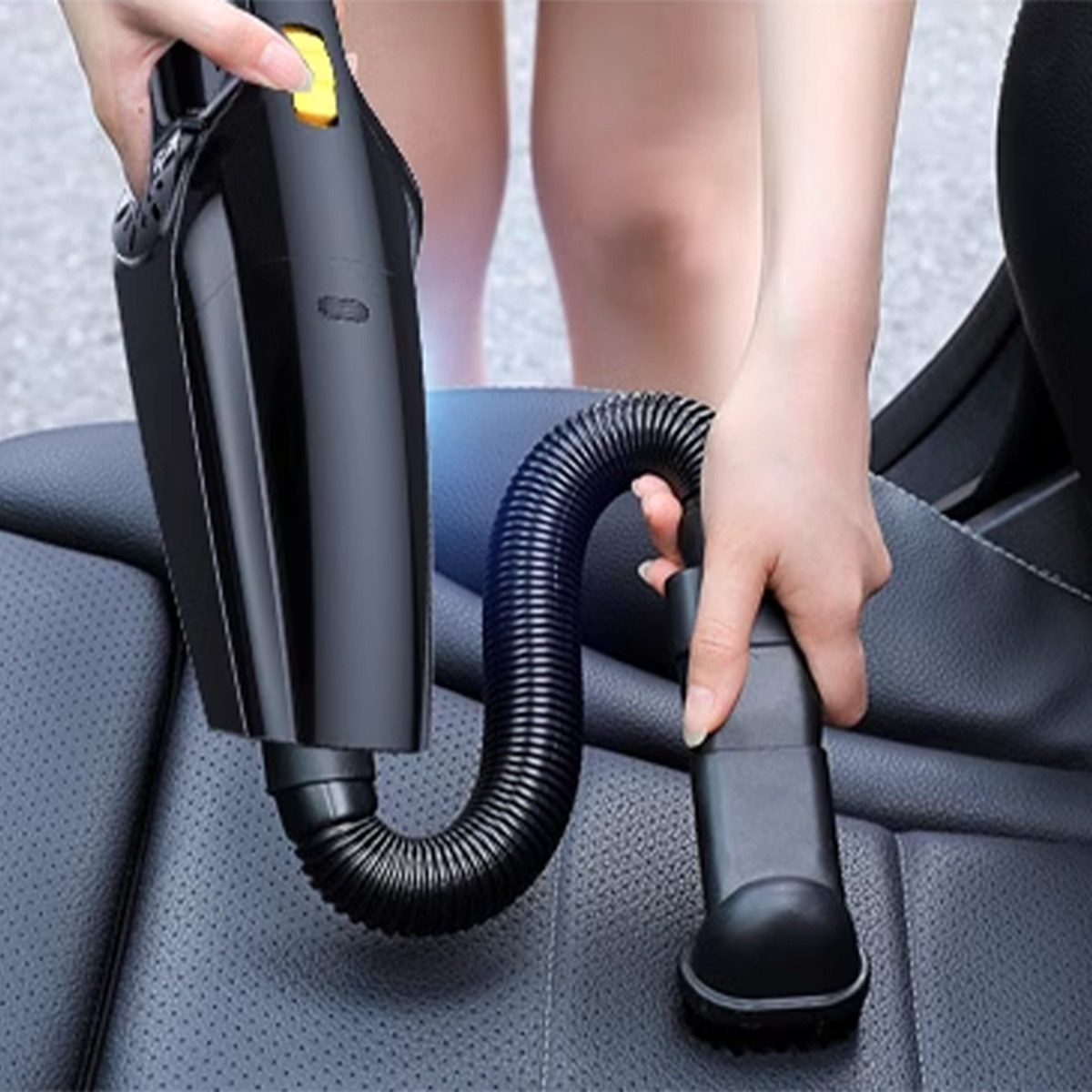 Eine Person saugt einen Autositz mit einem schwarzen Handstaubsauger. Der Schlauch ist flexibel.