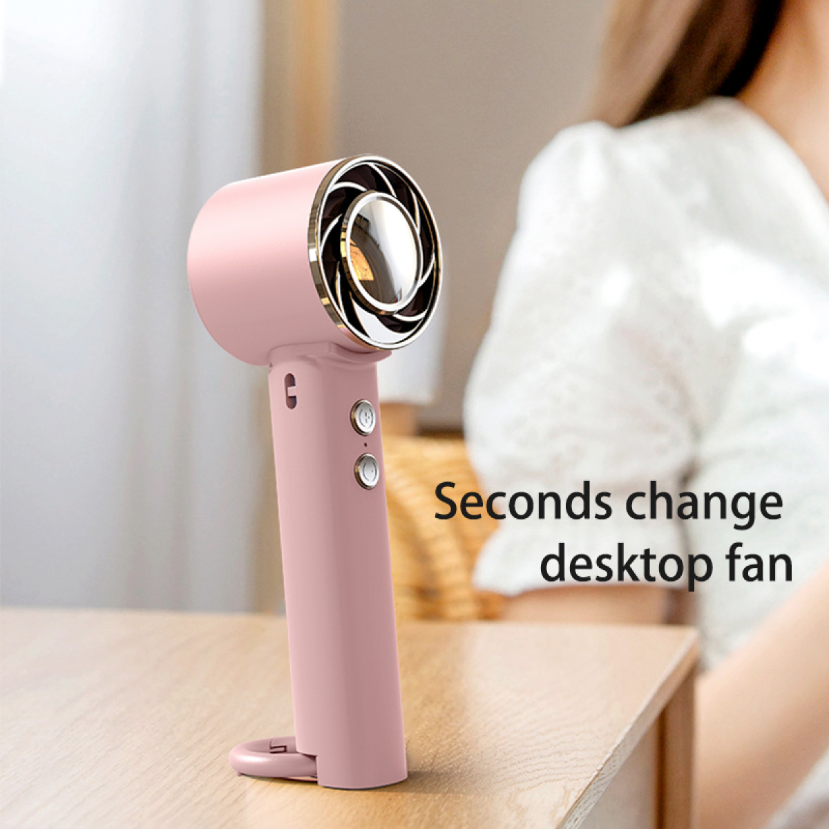 Een roze mini-ventilator op een tafel. De schouder van een vrouw is op de achtergrond.