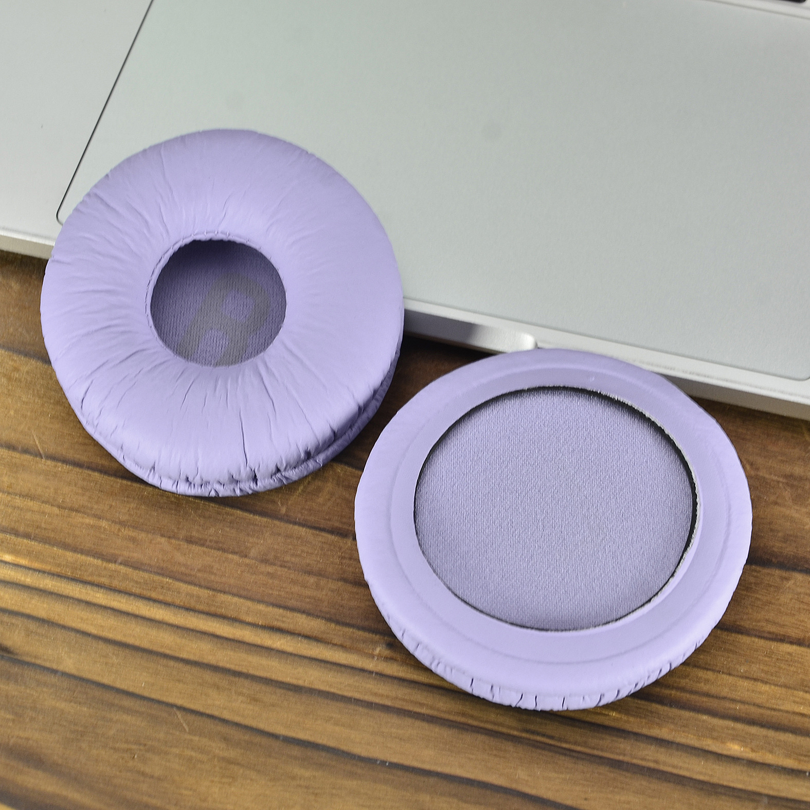 Zwei lilafarbene Ohrmuscheln auf Holzoberfläche, neben einer Laptop-Tastatur. Eine ist im Fokus.