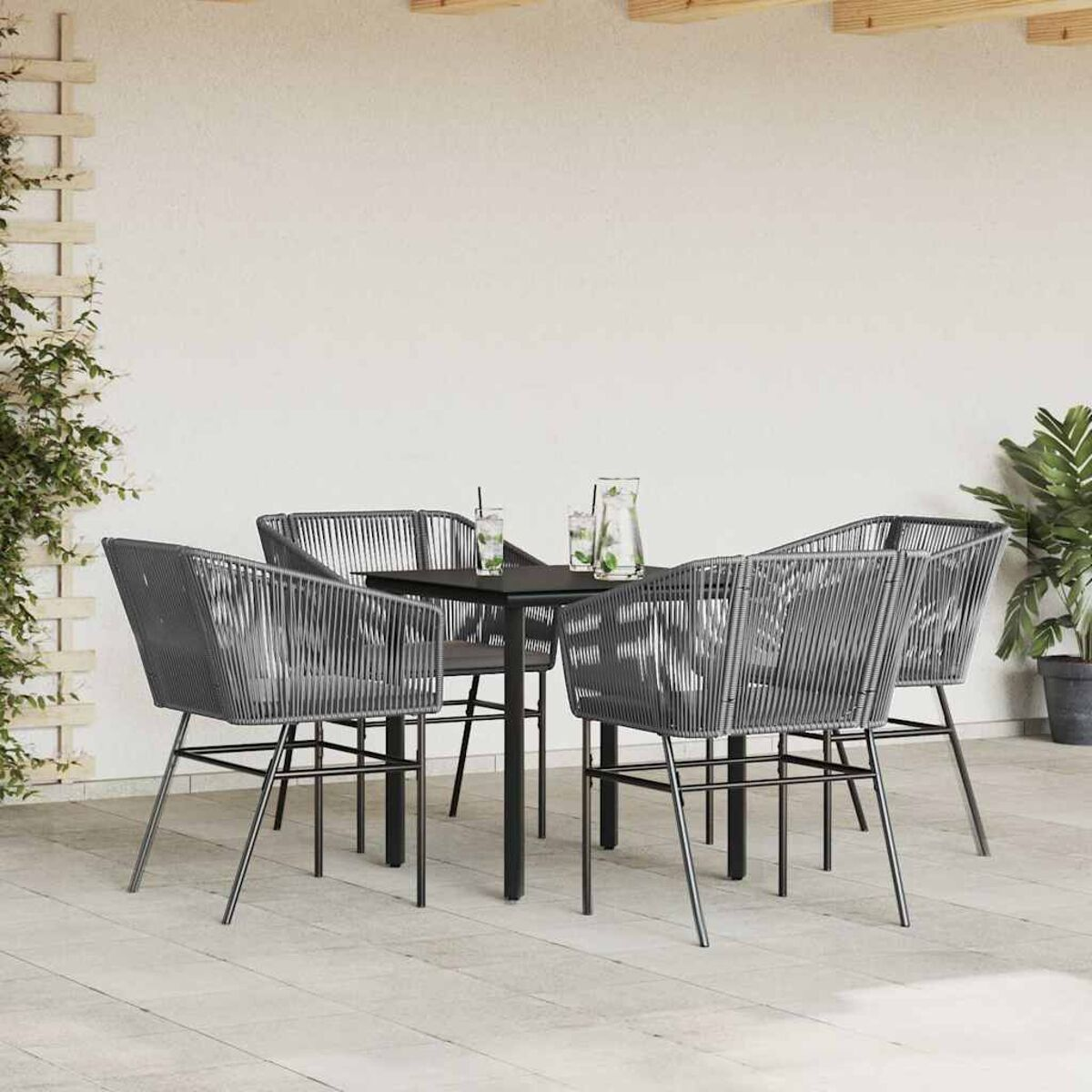 Set da pranzo all'aperto con sedie grigie e tavolo nero. Piante e muro sullo sfondo.
