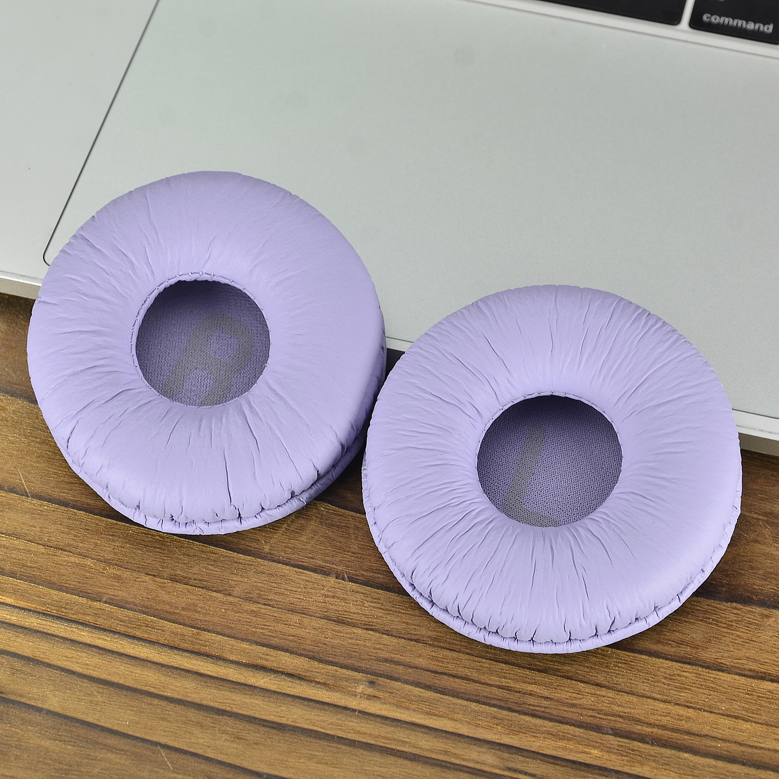 Zwei lavendelfarbene Ohrpolster auf einer Holzoberfläche und einer Laptop-Tastatur.