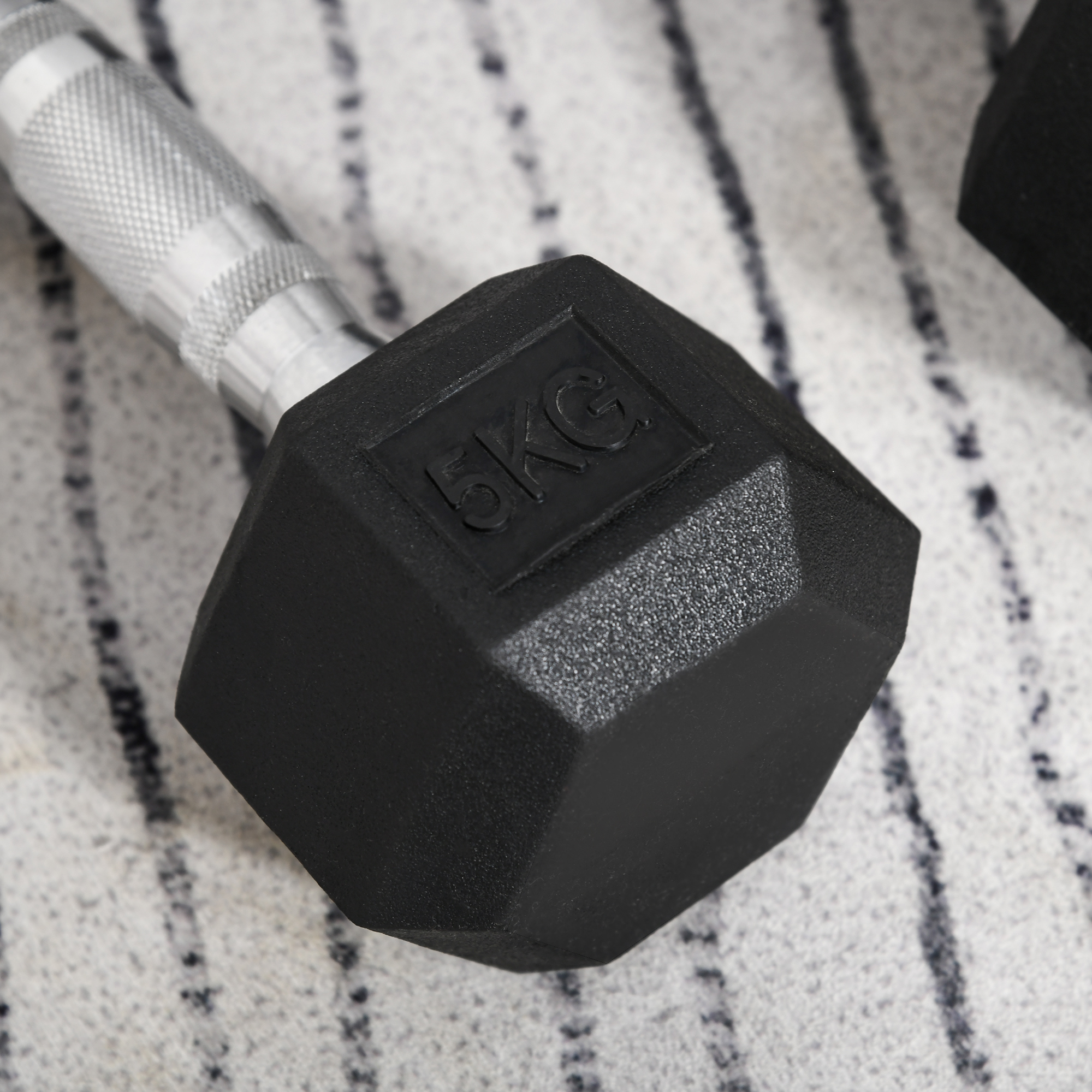 Schwarze Hantel mit sechseckiger Form, mit 5KG-Markierung, auf gestreiftem Hintergrund.